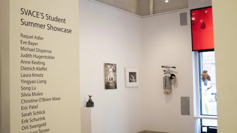 View of the entryway at the “SVACE Student Summer Showcase” at the Flatiron Project Space, 2023. There is a list of names on the wall of the participants in the show. Three sculptural pieces are seen, and two artworks framed on the wall are seen.