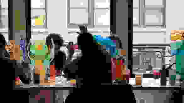 Artists paint on lucite panels while sitting down at a work table.