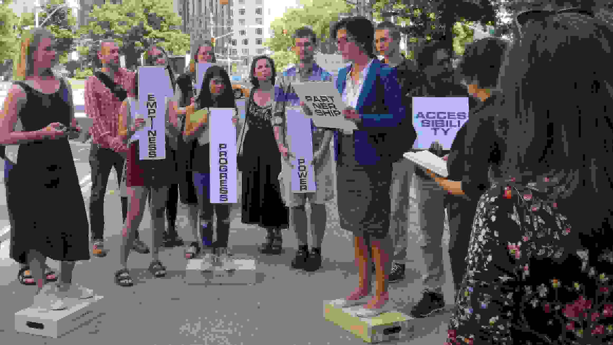 Group of students standing on platforms outdoors, holding placards marked with various design concepts