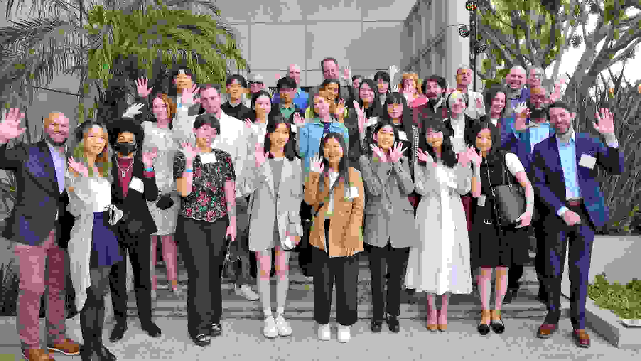 A group of graduates from SVA's class of 2022 and SVA staff members pose in on a set of stairs, smiling and waving at the camera.