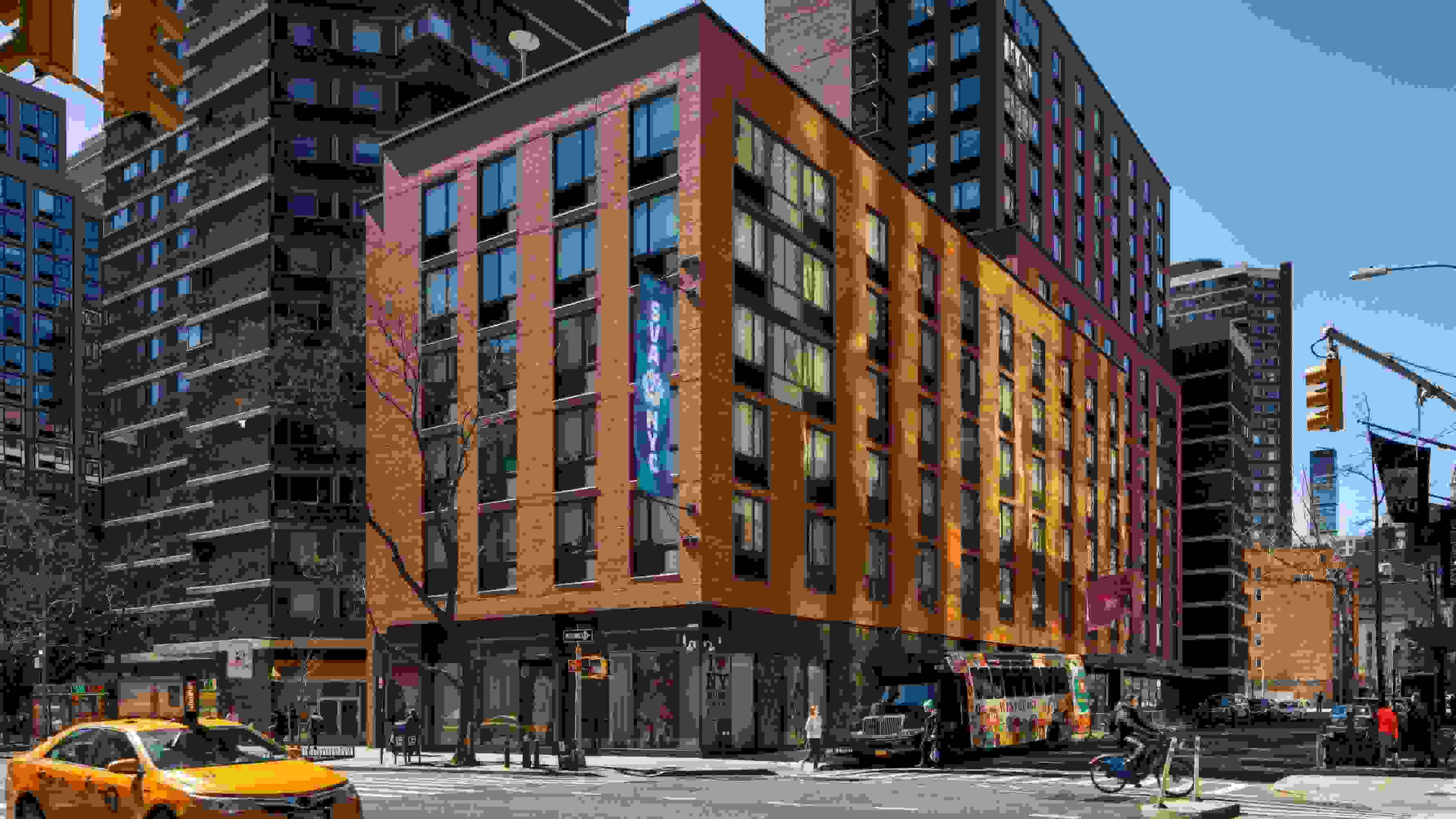 A busy New York City street; a building facade with an ‘SVA’ flag on it.