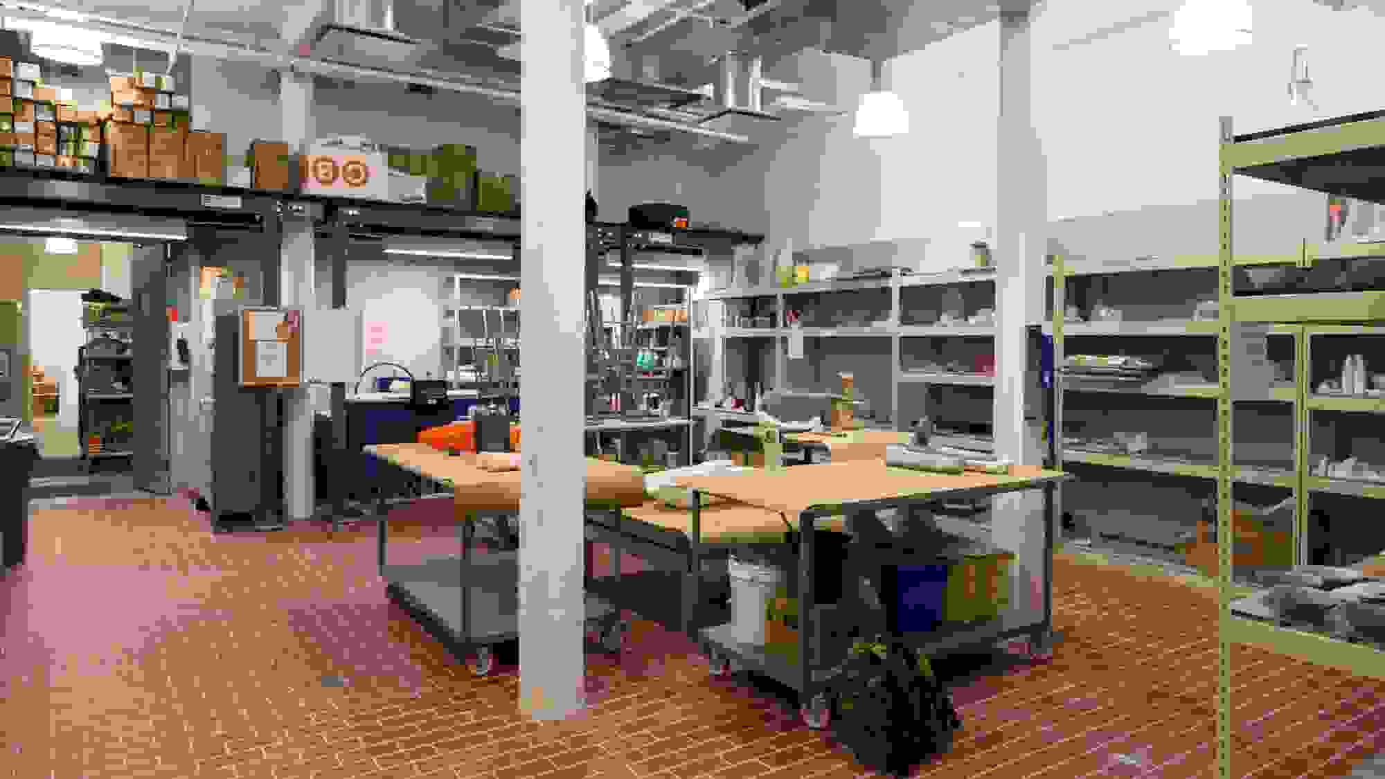 Wide view of a ceramics studio with red brick floors and drying racks.