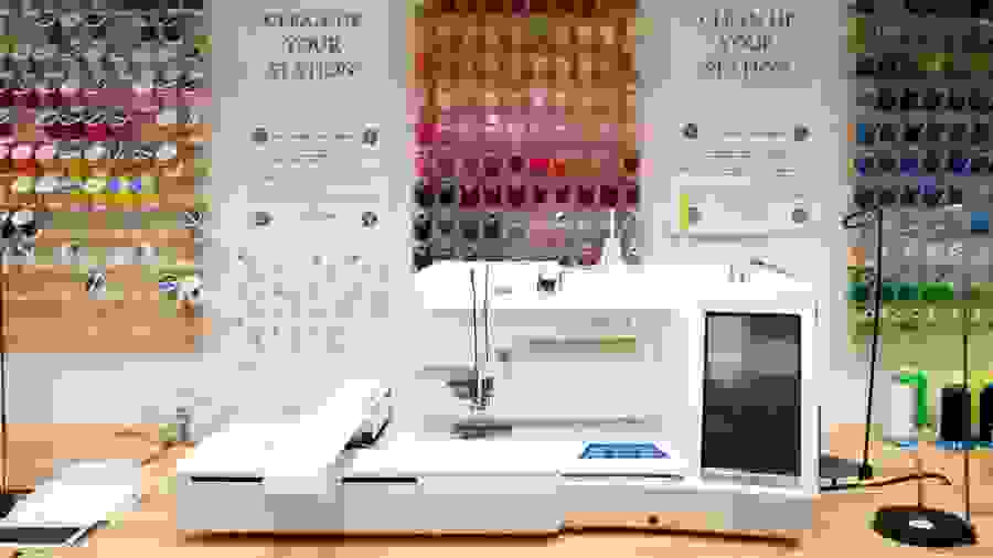 Fabric studio view of a professional grade sewing machine and various colored spools of thread hanging on the wall.