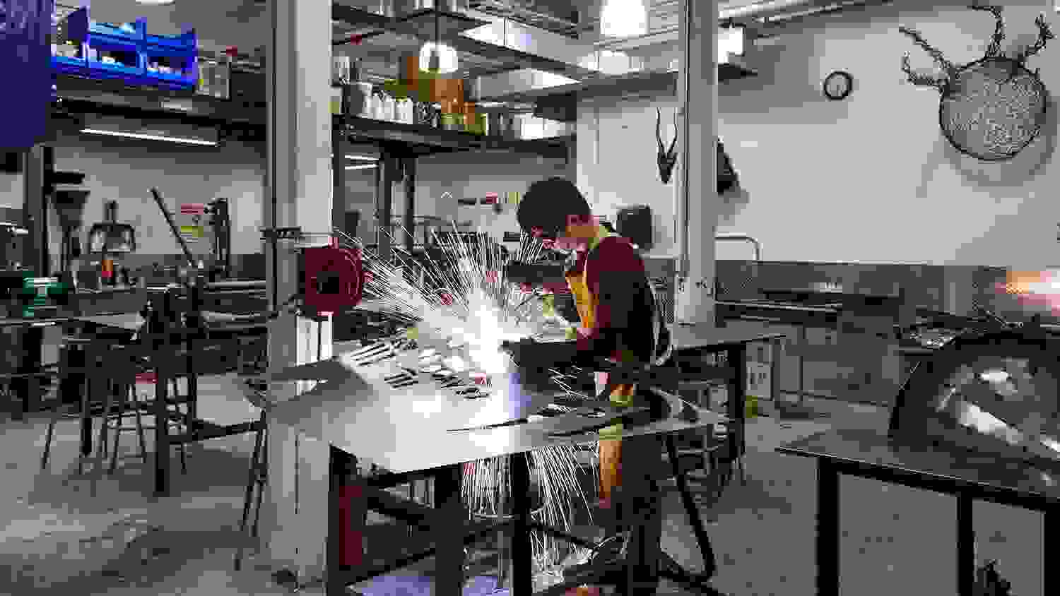 Student wearing protective goggles while metalsmithing; sparks are flying everywhere