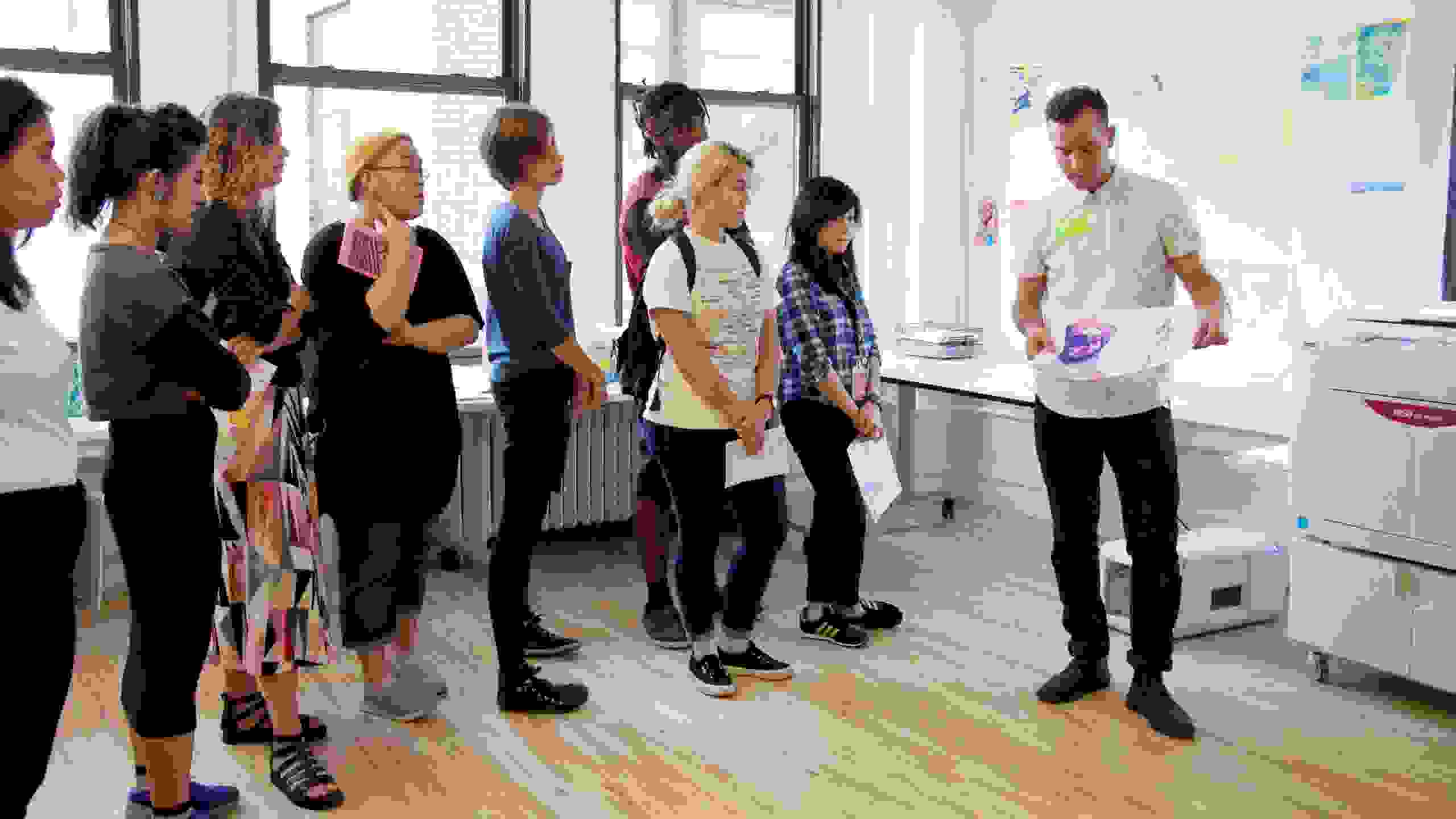 A classroom of students watches as an administrator shows the finished product of a risograph print.