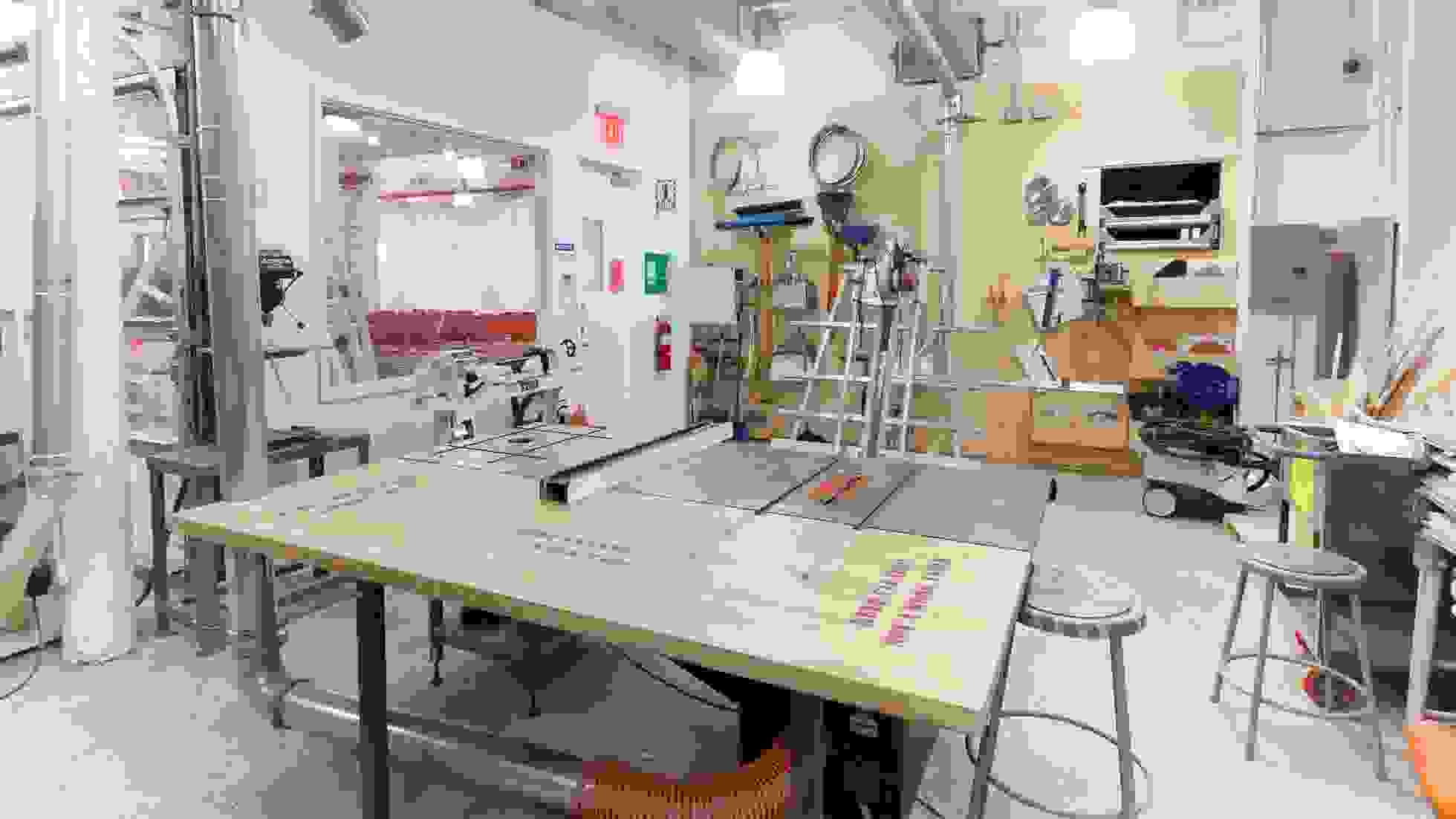 Interior of a woodshop with benches, equipment and metal stools.