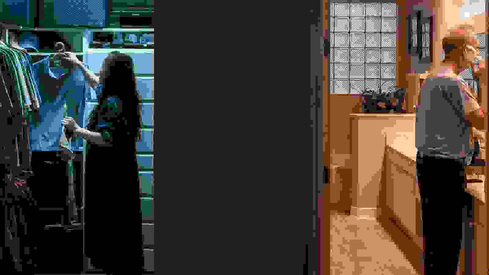 A dark wall in the middle of the image divides this color photograph into three equal parts. In the left third we see into a closet where an Asian woman is putting away a shirt in cool blue light. In the right third a white man is shaving in a bathroom lit by warm light. 