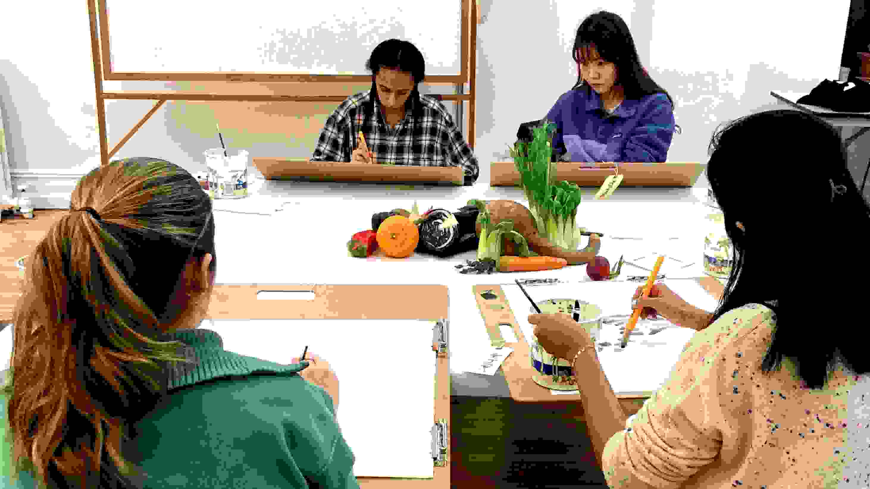Photograph of four students drawing a still life of various fruit
