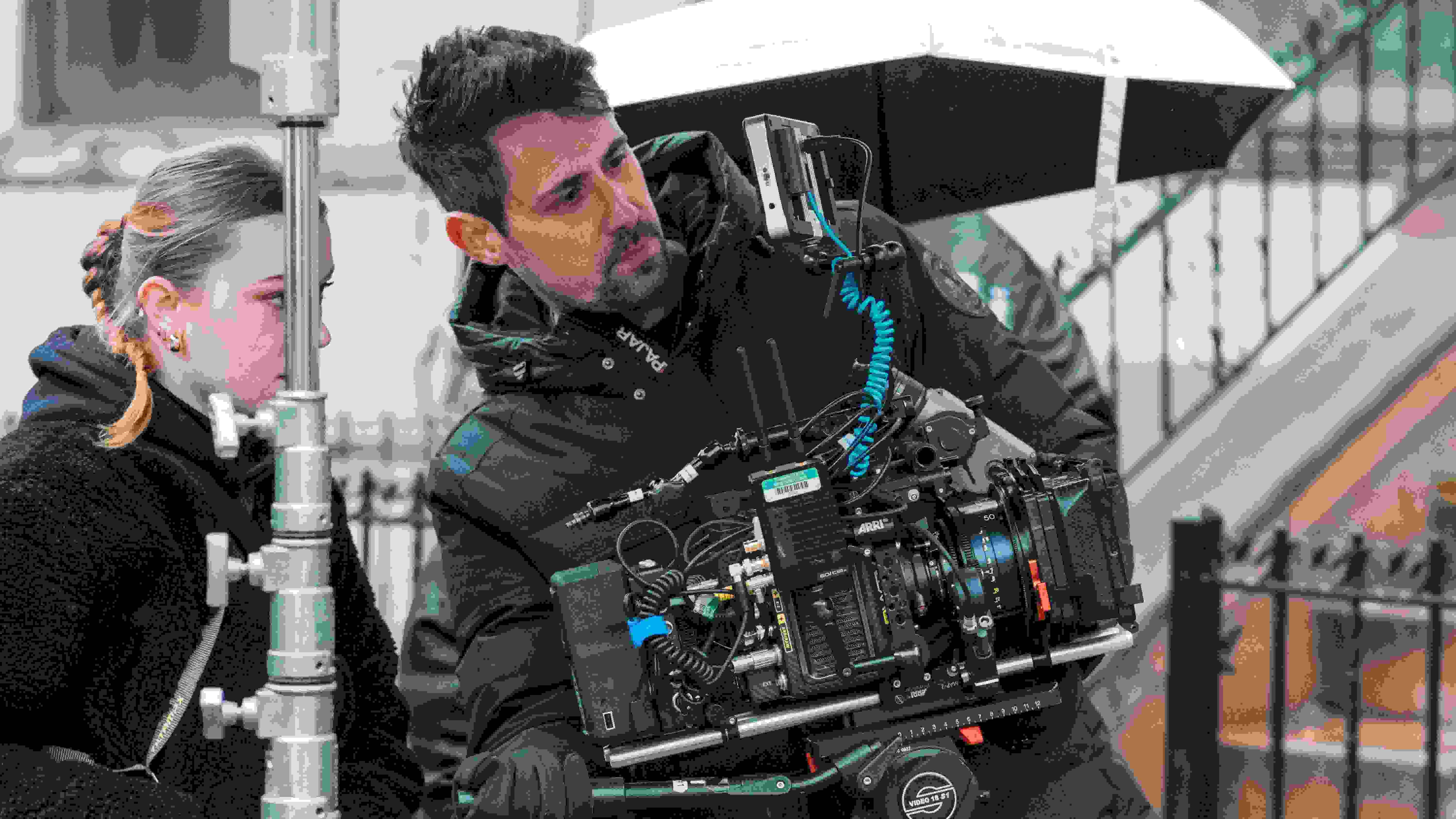 Photograph of two people, a cameraman holding a sophisticated digital film camera, the other directing the cameraman