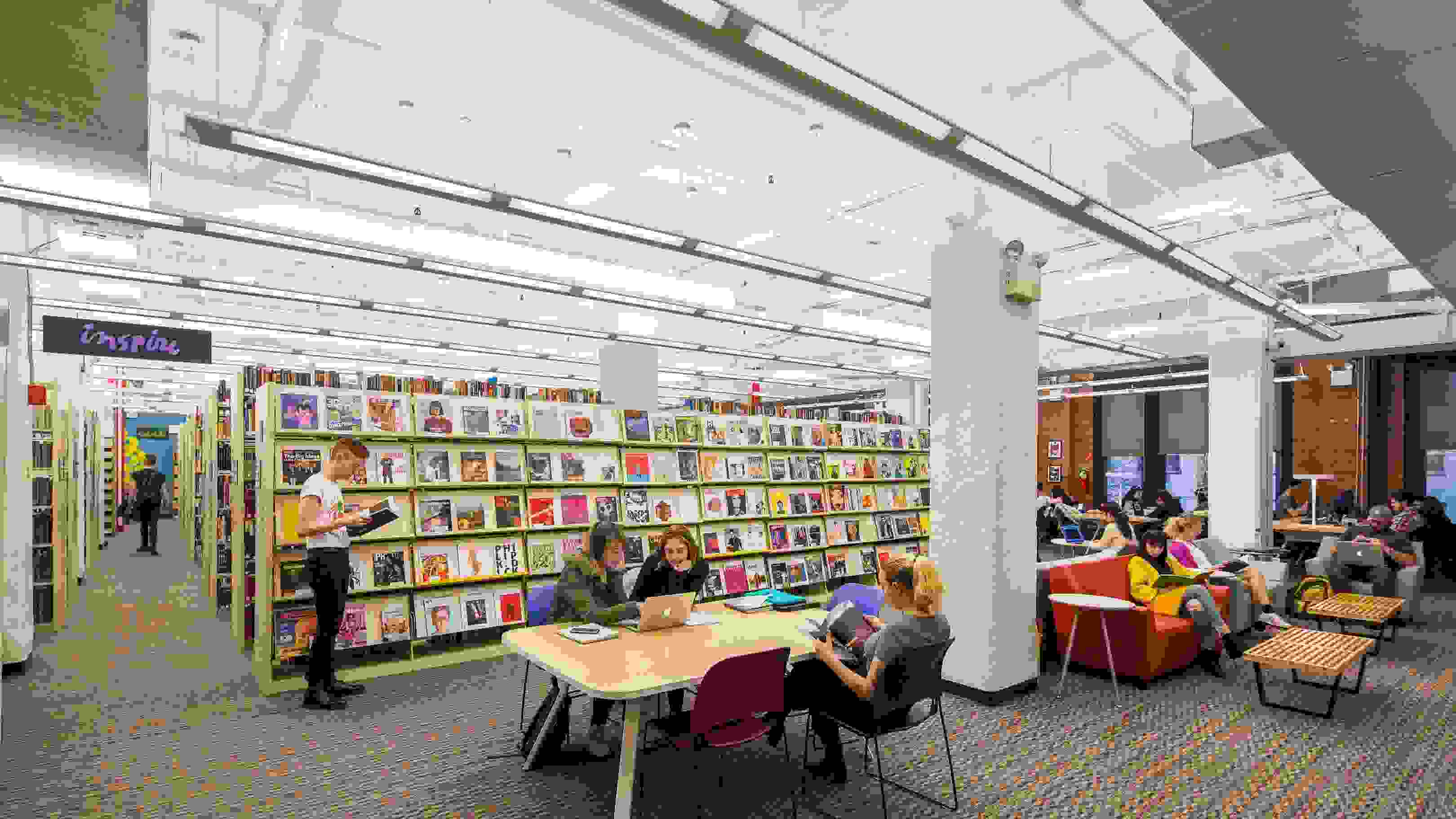 interior view of a library with stacks, study tables, couches and students working with one another