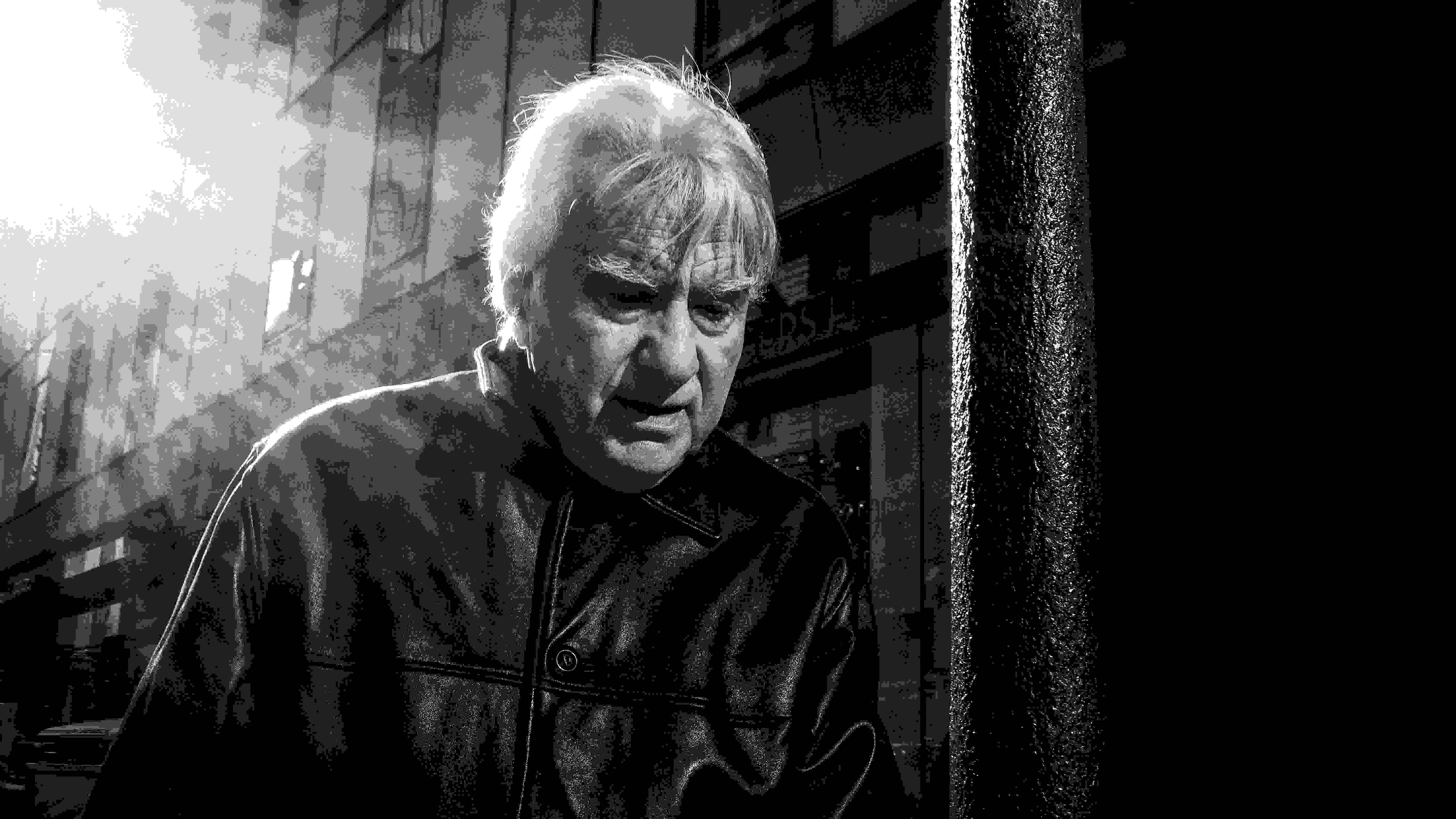 A black-and-white photograph of a man walking through the street. The sun shines over his shoulder.