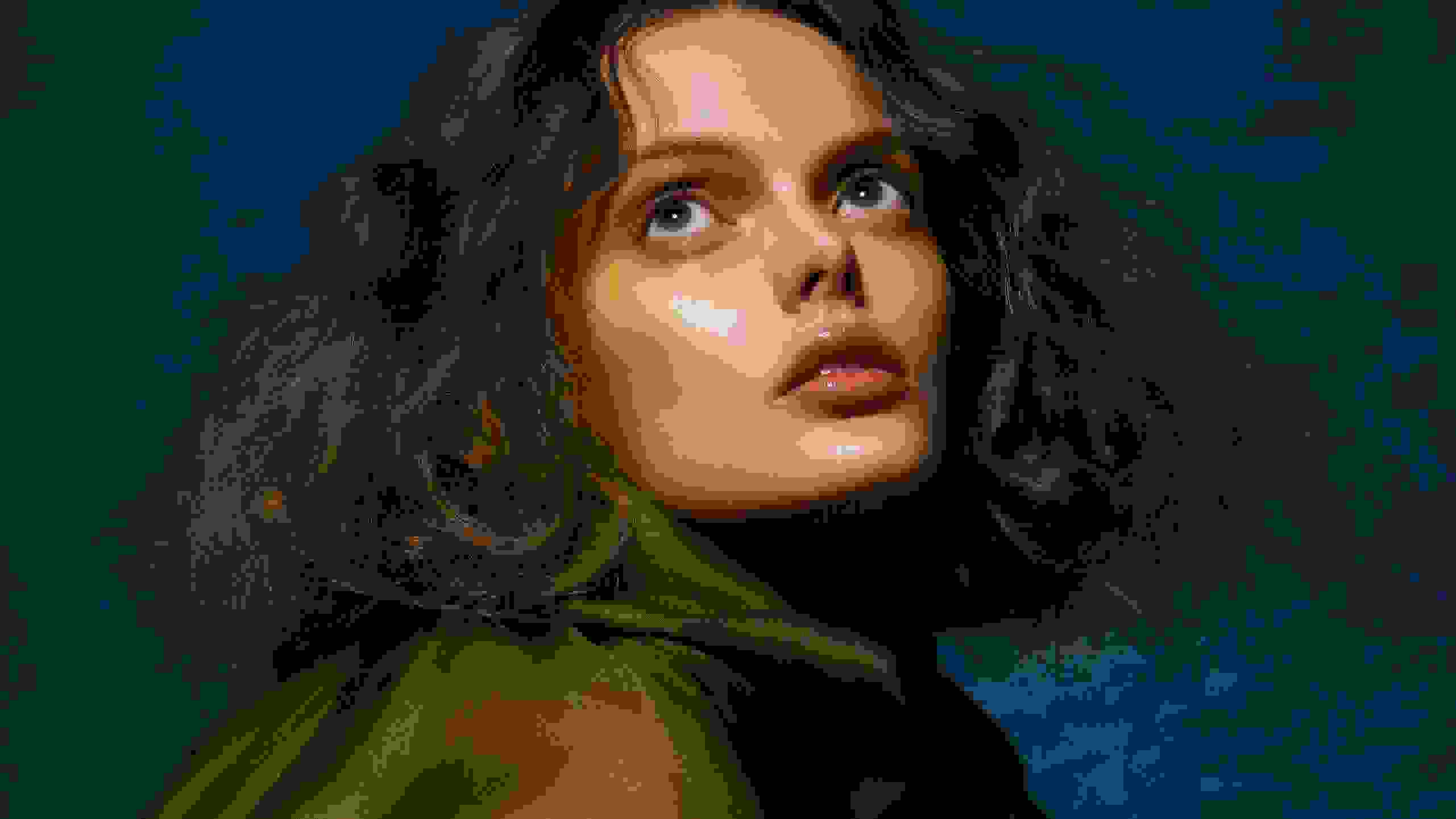 A fashion portrait of a woman against a blue background. She has shoulder length, wavy hair, is wearing a sheer green drapery, and looking up and off camera.