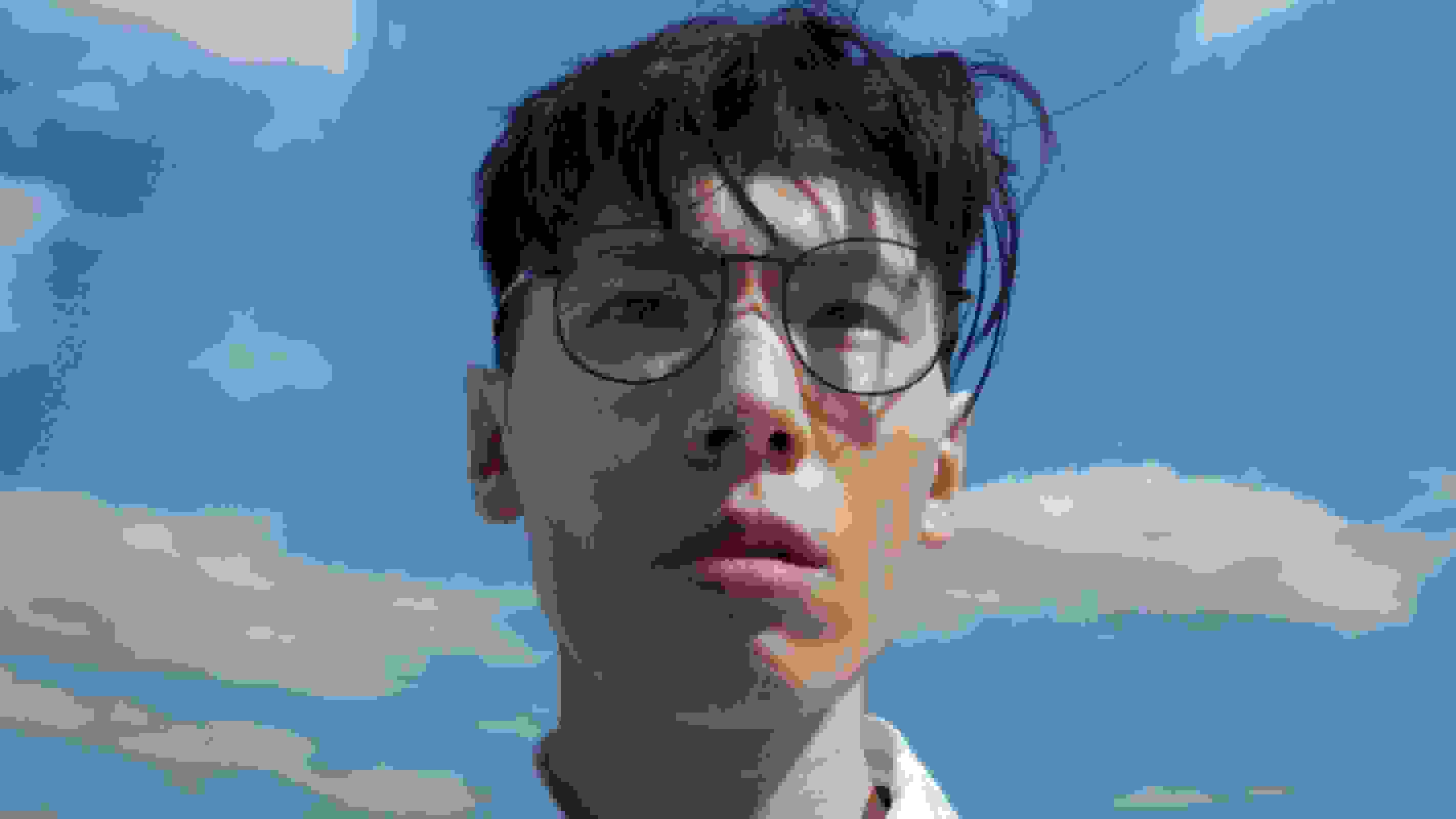 A close-up of a man's face looking off-camera. Behind him is a blue sky with clouds.