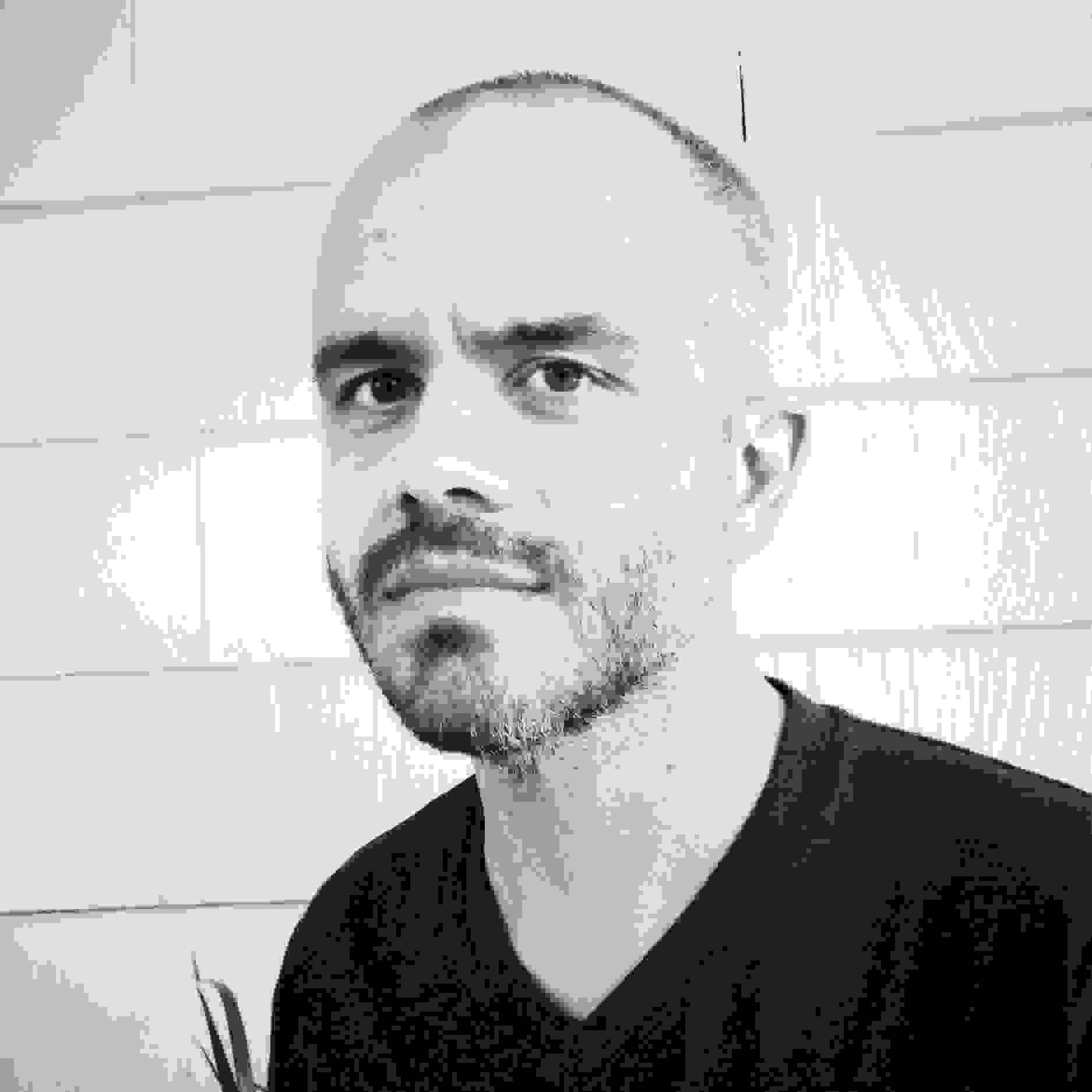 Head shot of Adam Bell, man with short dark hair and closely-cropped beard in black v-neck t-shirt