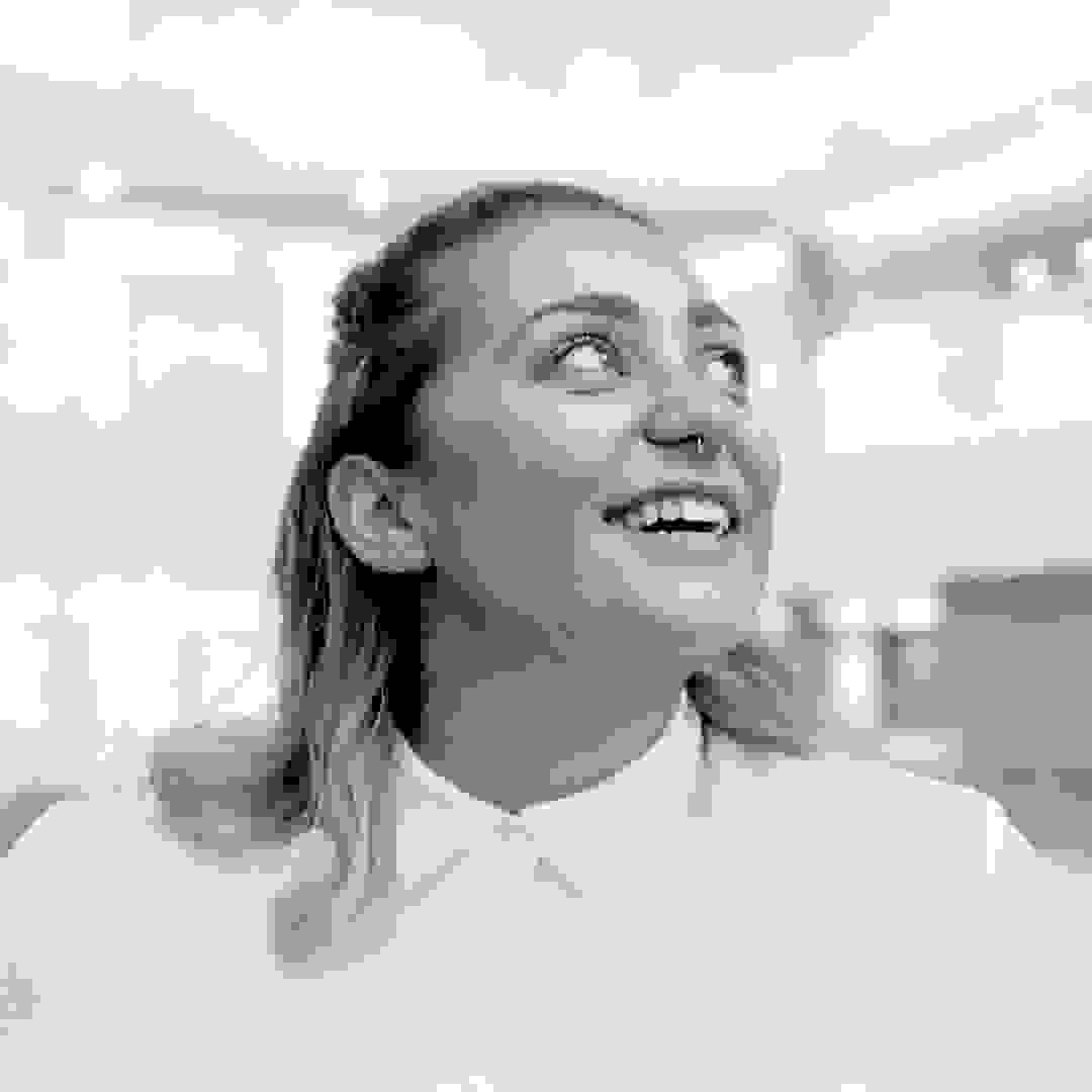 Black and white headshot of Amelia Nash. She is wearing a white button-up blouse, smiling, and looking upwards.