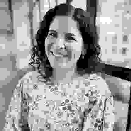 Black and White headshot of a woman with dark curly hair, wearing a floral dress.
