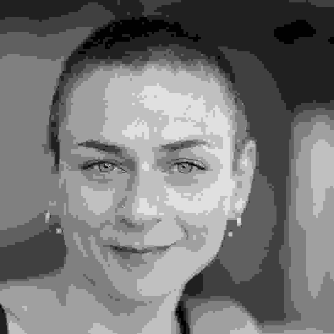 A portrait of Julie Grahame, who is looking into the camera with a smile. Julie has short hair and a nose pierce. 