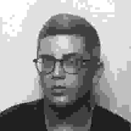 Black and white photo of white person with short graying hair, wearing round glasses, not smiling, looking at camera.