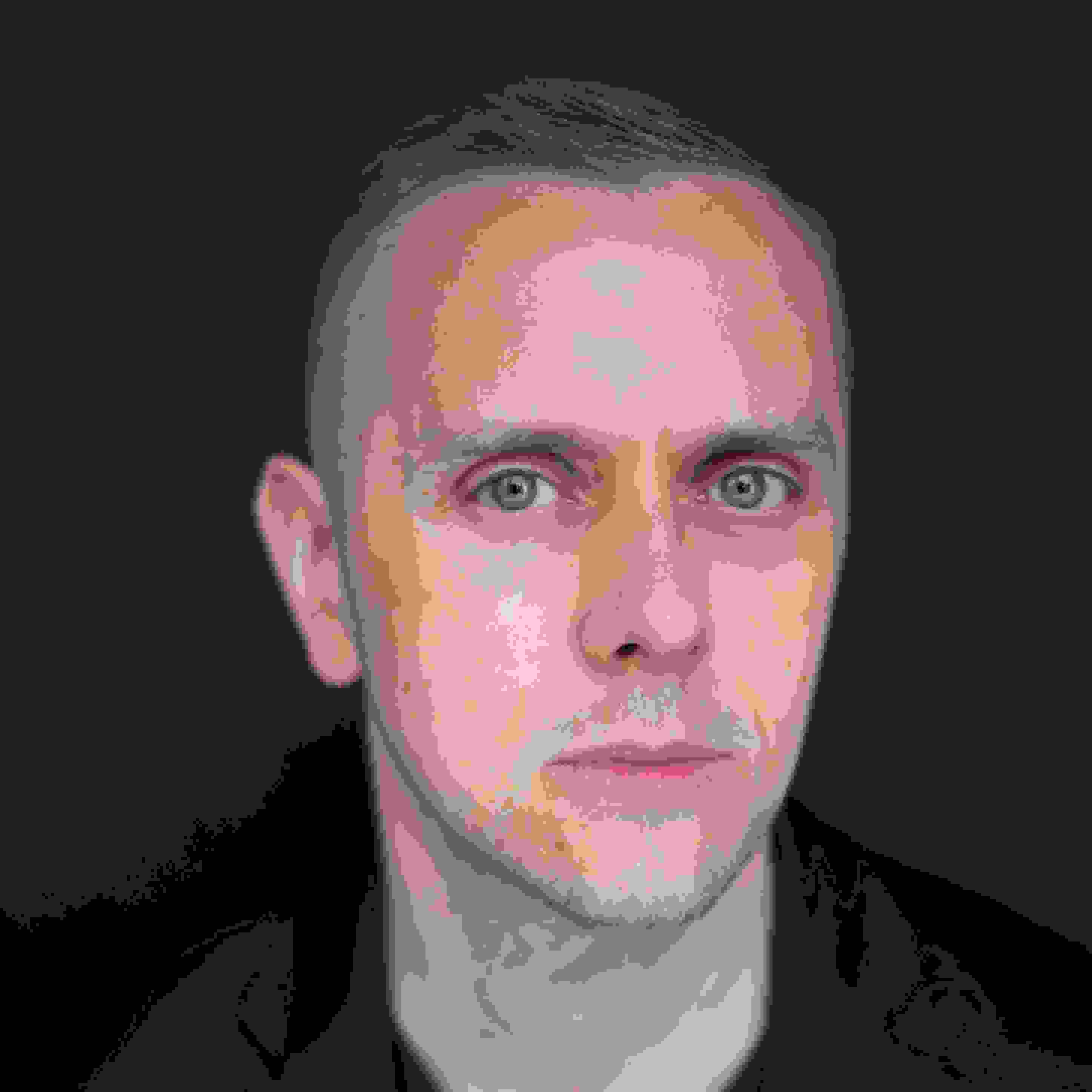 A portrait of Marko Kovacevic looking into the camera against a black background. He has short, blond hair and blond beard. 