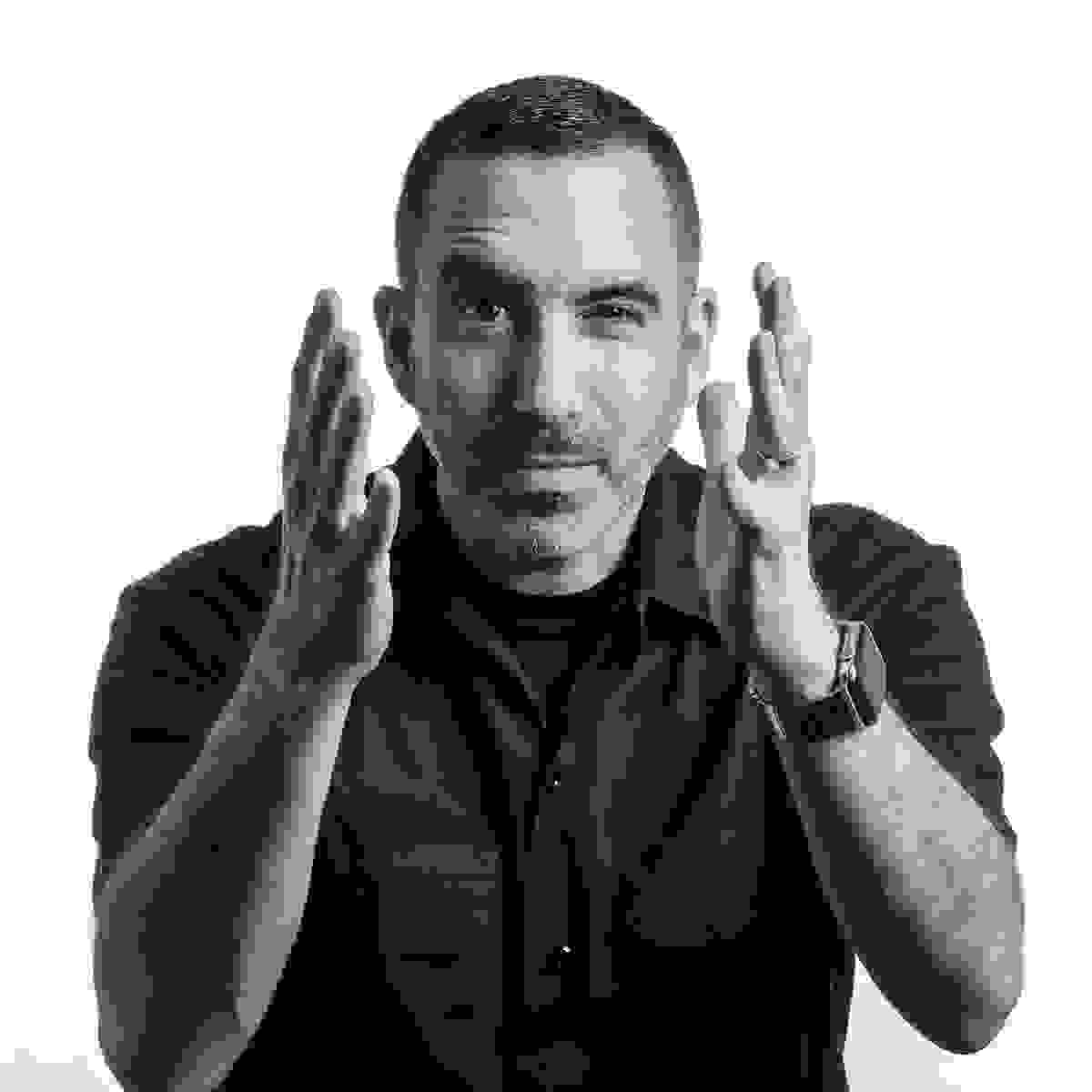 Black and white portrait of a middle-aged man with short dark hair and facial stubble, wearing a dark button-up shirt.