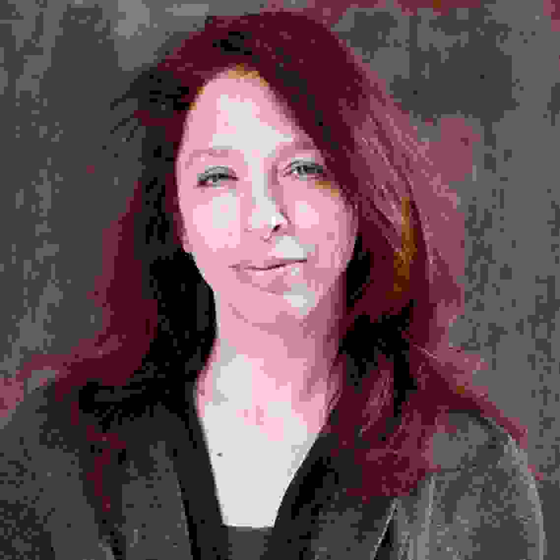 Image of a woman looking at the camera. The woman has red hair and is wearing a gray top.