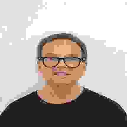 Portrait of John Ruggeri wearing a black shirt and black frame glasses.