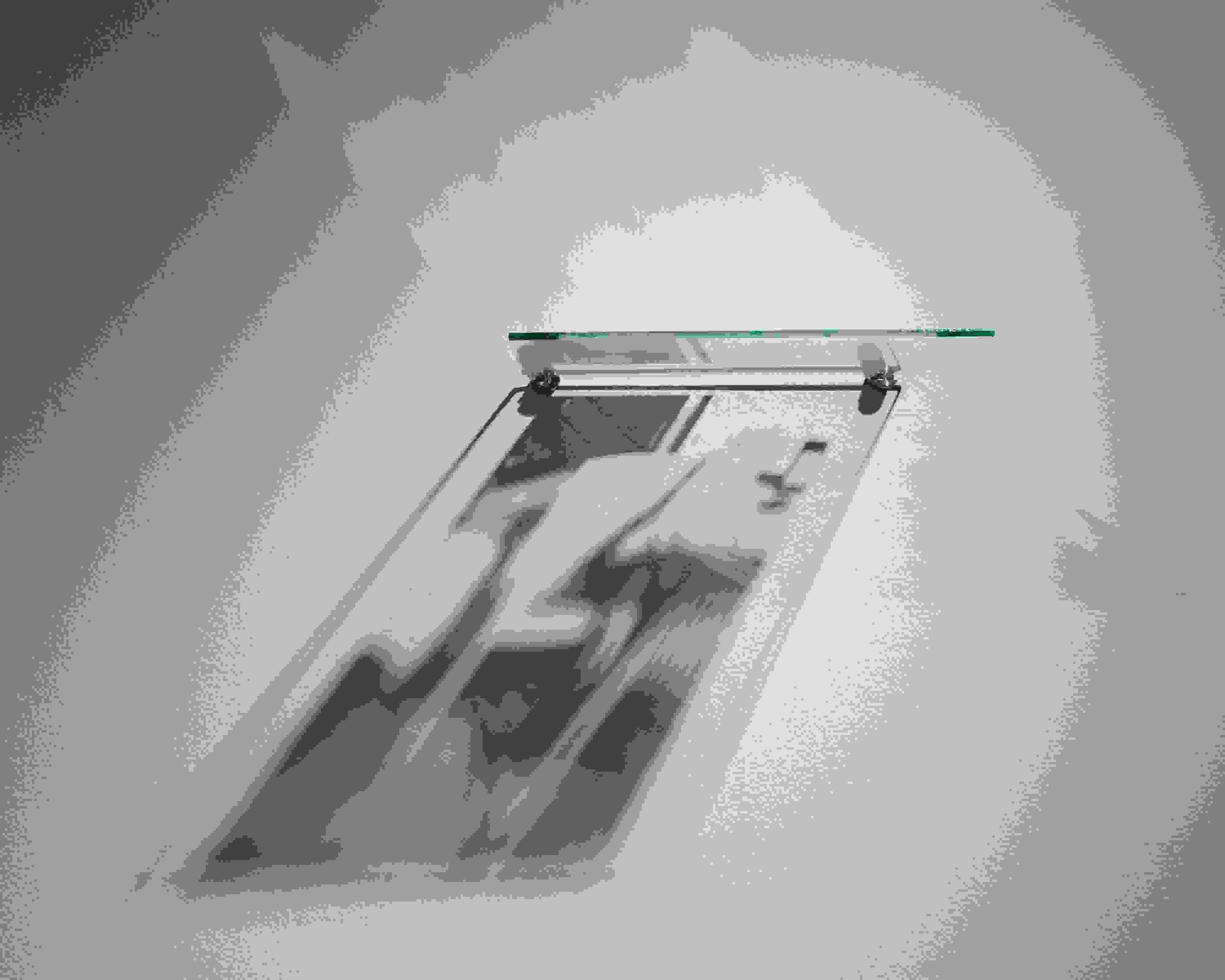 A wall-mounted, silkscreened pane of glass, lit from above, creates a shadow-based image of a lawn chair below it.