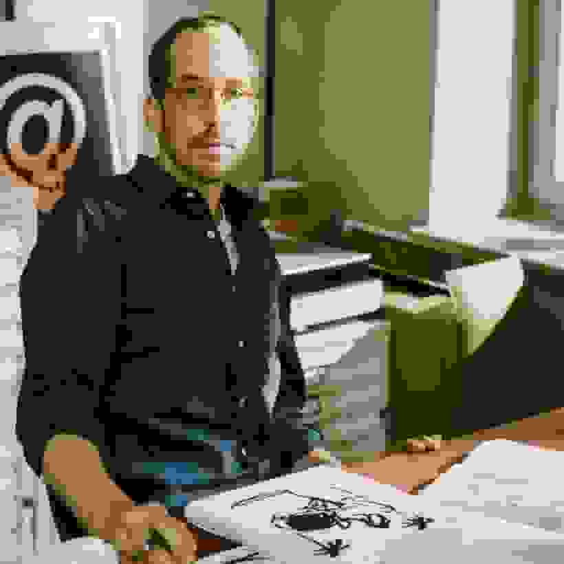 An artist looking into the camera, there is a drawing in front of him