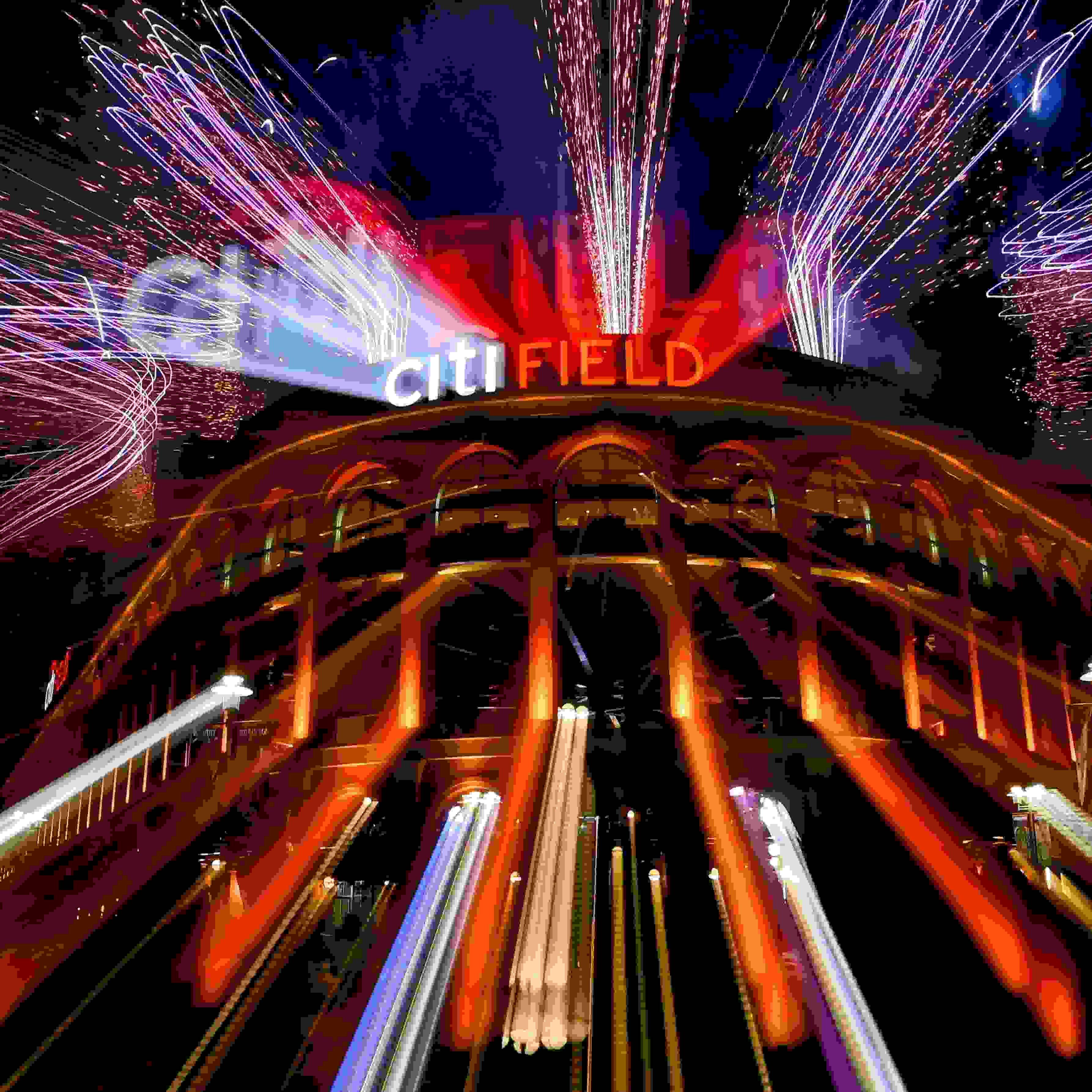 A photograph of Citi Field, the home stadium of the New York Mets, at night. There are bright, colorful lights and fireworks going off.