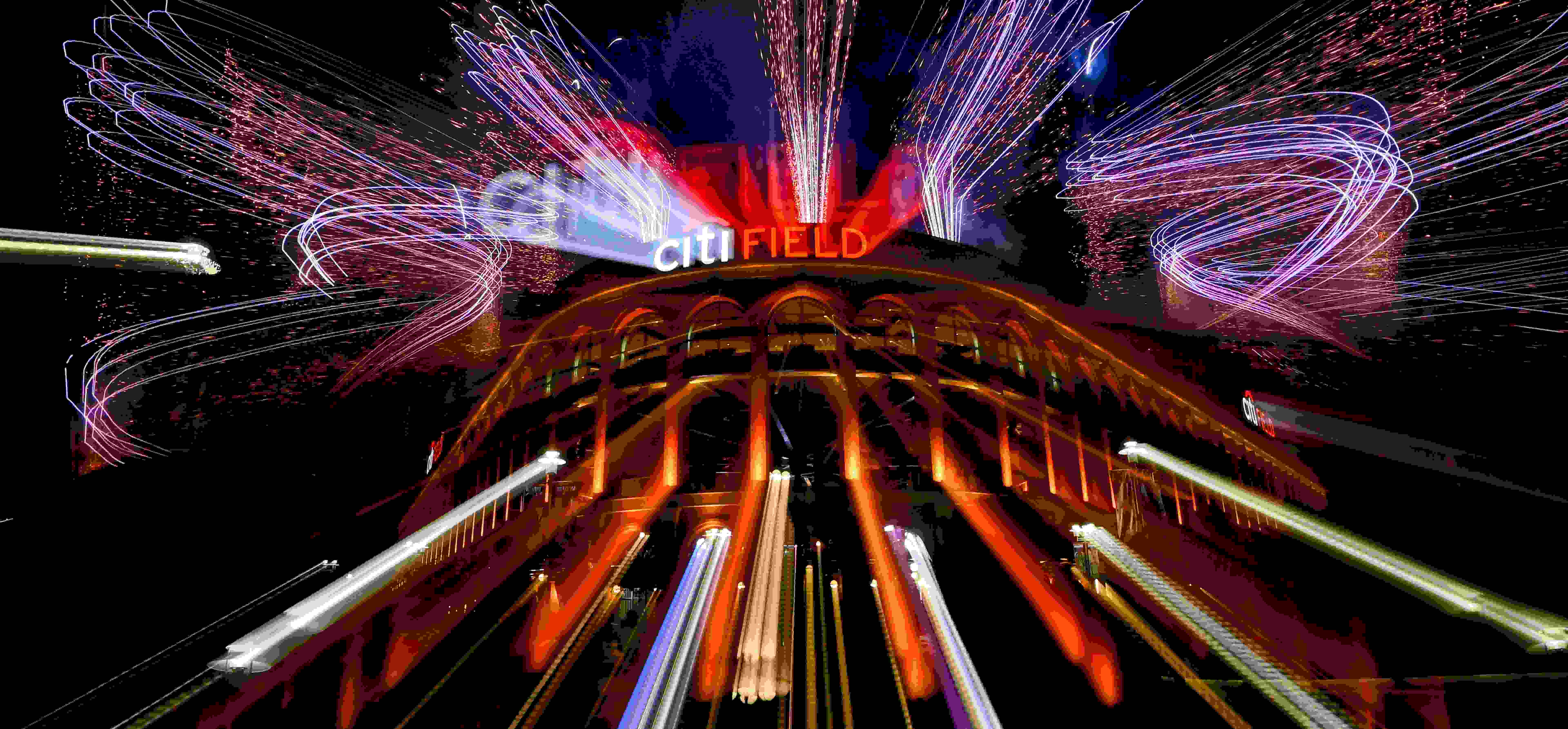 A photograph of Citi Field, the home stadium of the New York Mets, at night. There are bright, colorful lights and fireworks going off.