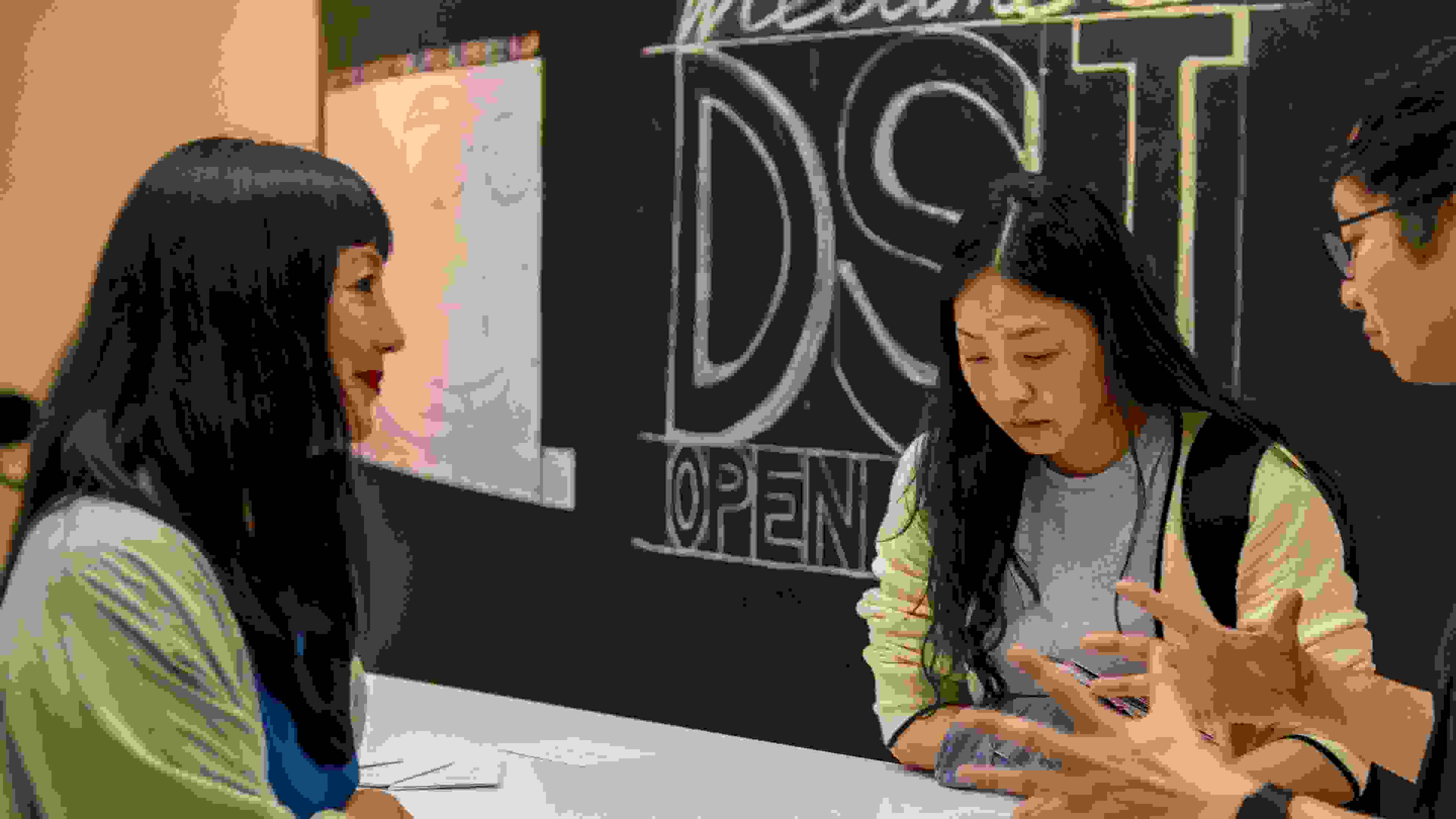 a person with long dark hair on the left looking at 2 students speaking.