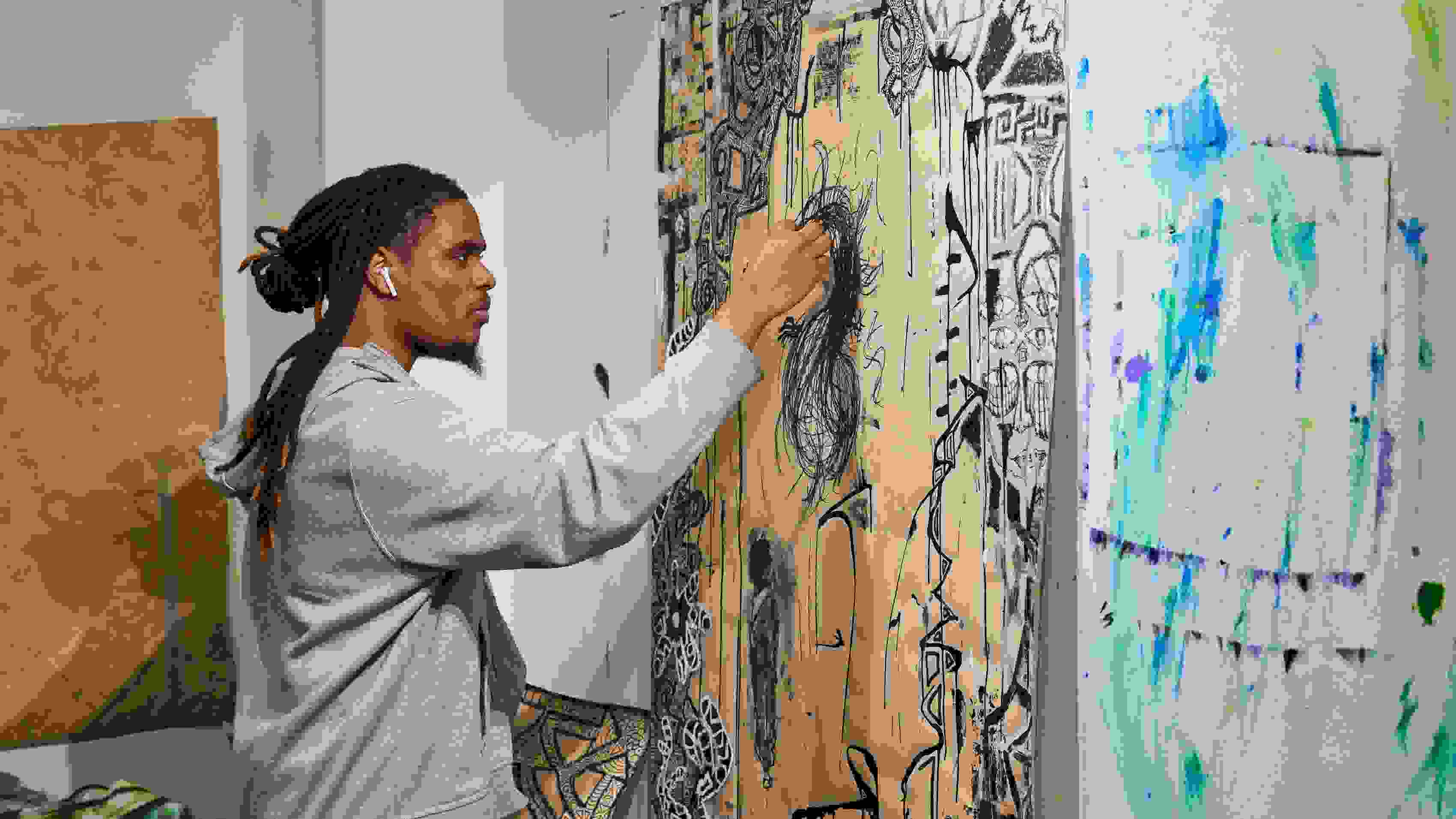A person in a gray hoodie wearing air pods works on a wall mural
