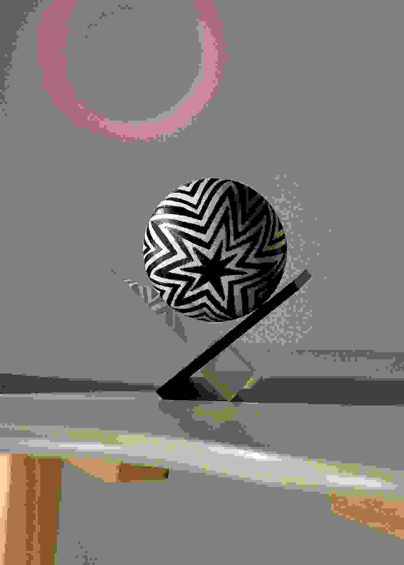 Rendering of three simple objects—a pyramid, a sphere suspended on an acrylic frame, and an iridescent cube—rest on a bean shaped table.