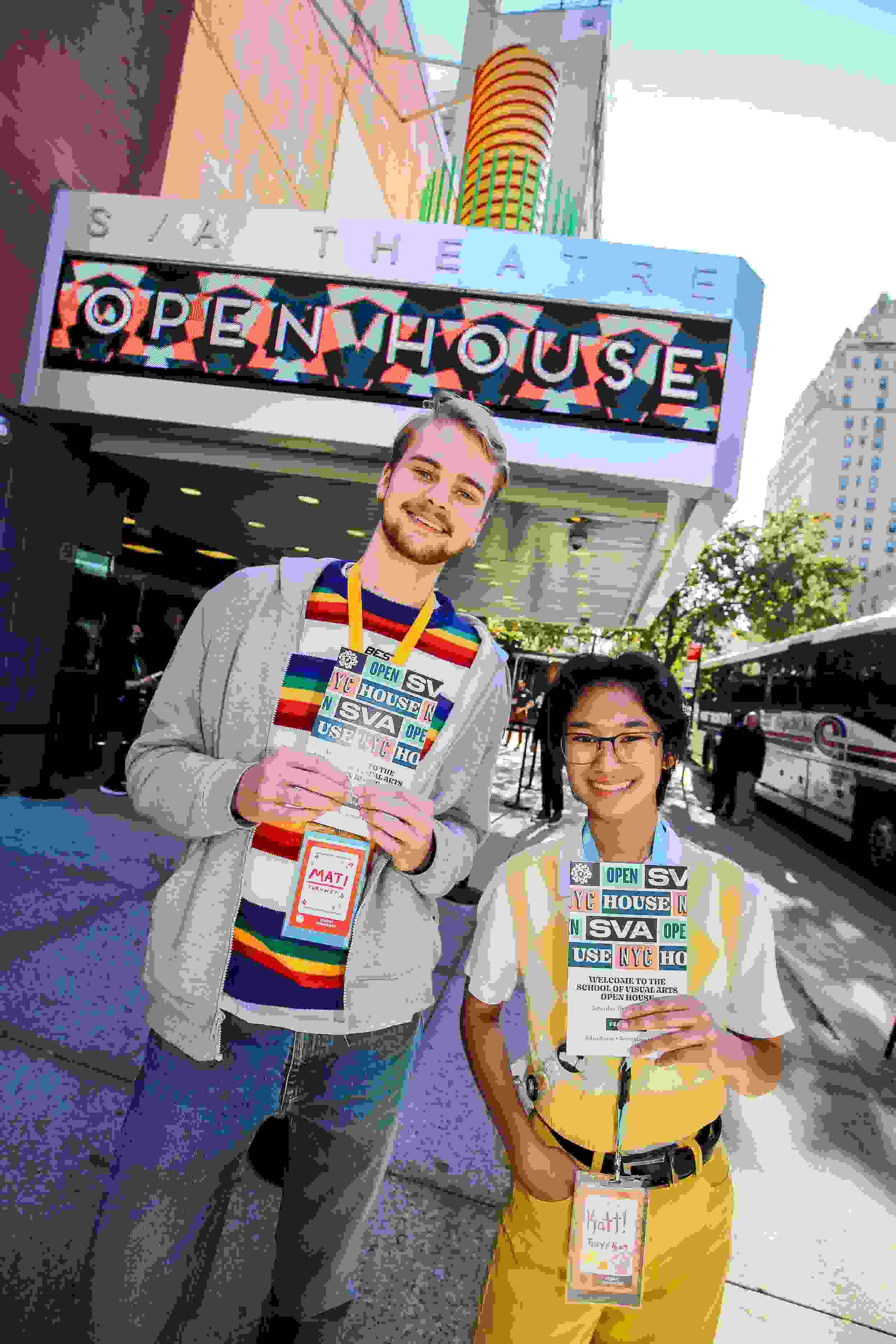 Two student ambassadors wearing bright colors stand in front of a theater