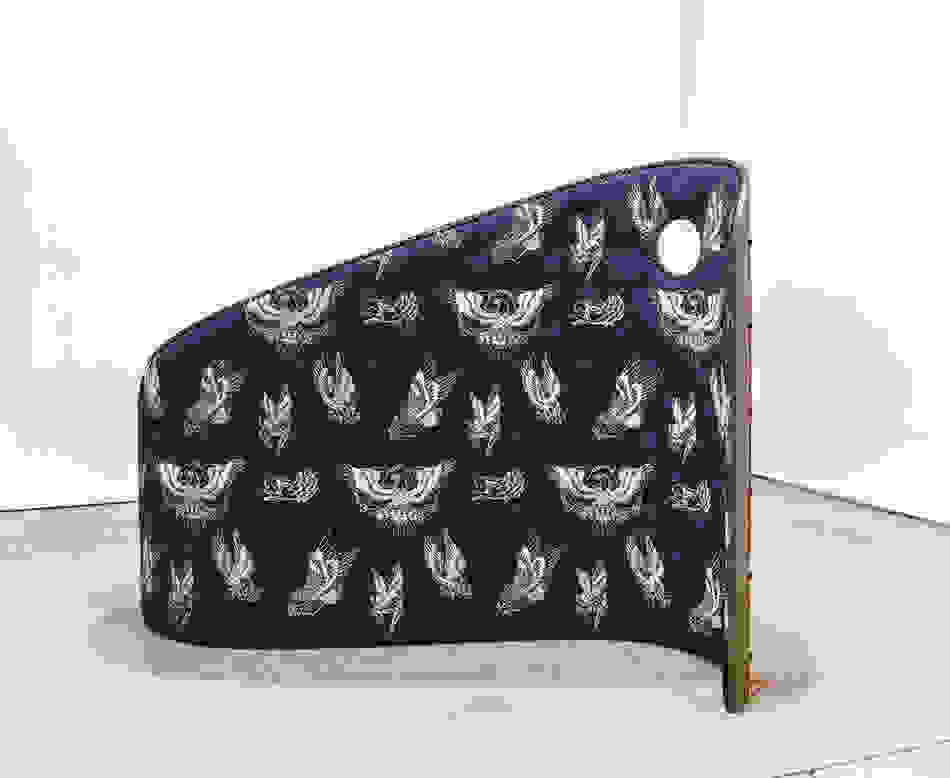 <p "="">A curving, wall-like sculpture upholstered in blue tufted denim that has been printed with several images of birds, which have been rendered in white lines.