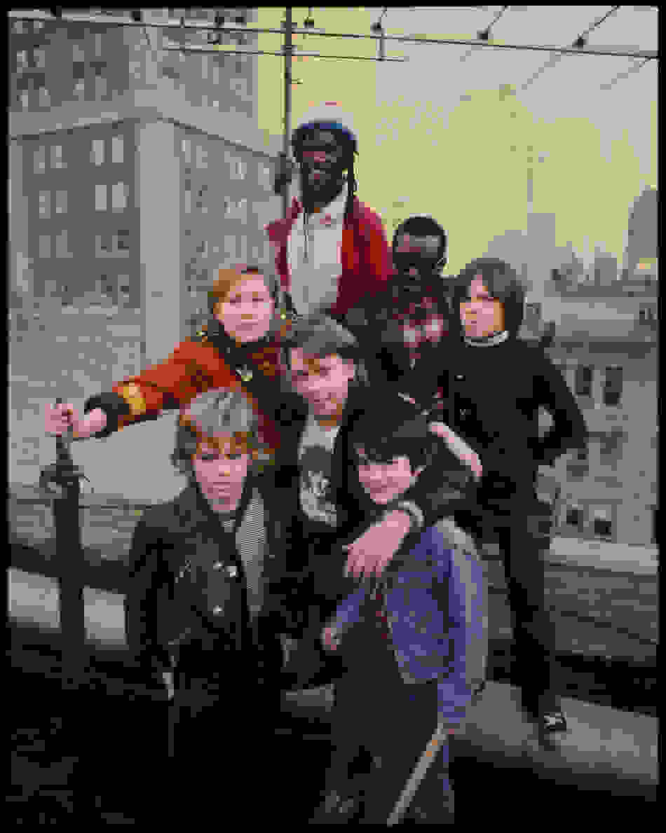 A color photograph of two men and five kids posing on a New York City rooftop.
