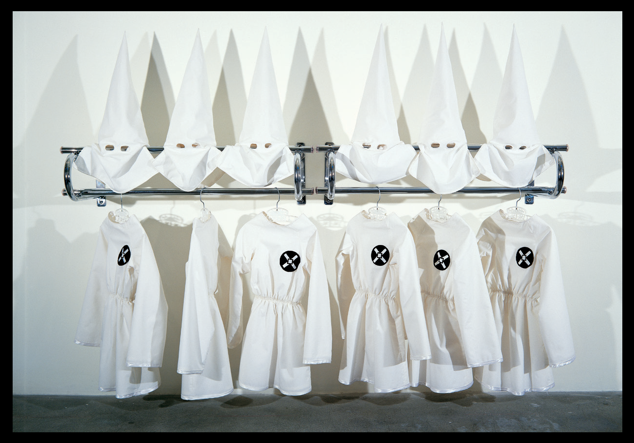<p "="">Six child-sized Ku Klux Klan cloaks and hoods arranged on a chrome coatrack.
	<br>