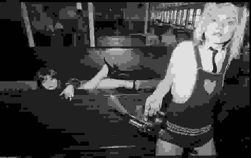 A black-and-white photo of two women on the Staten Island ferry, with the woman in the foreground holding a tommy gun.