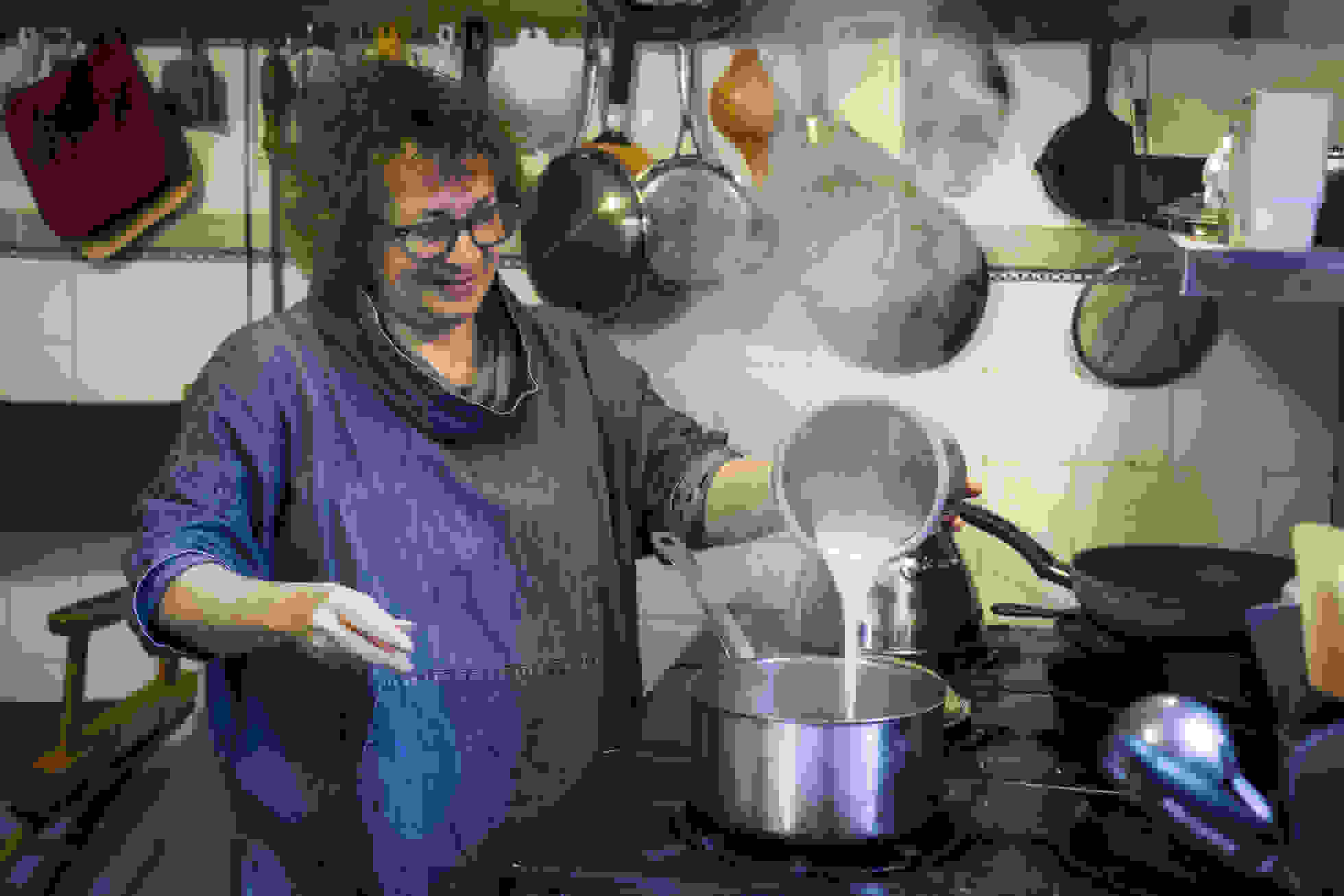 <p "="">A woman stands next at a stove, pouring steaming milk into a pot.
