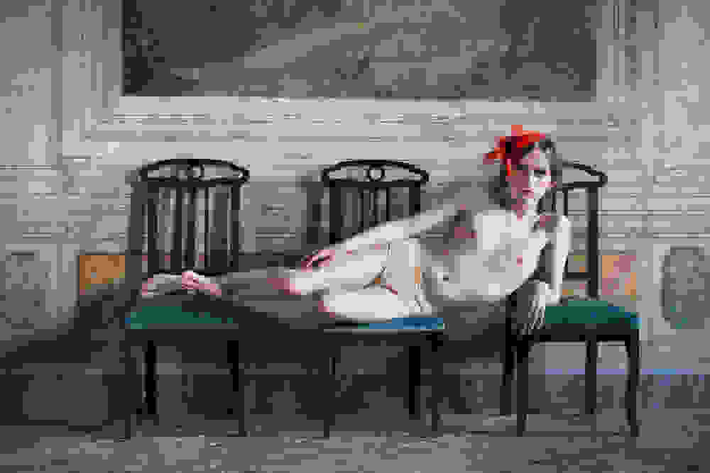 <p "="">A photograph of a person lying sideways across three dining chairs.