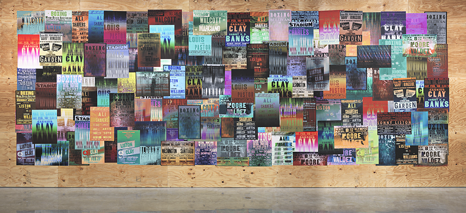 A large-scale collage of colorful, blurry reproductions of boxing posters on a plywood wall.