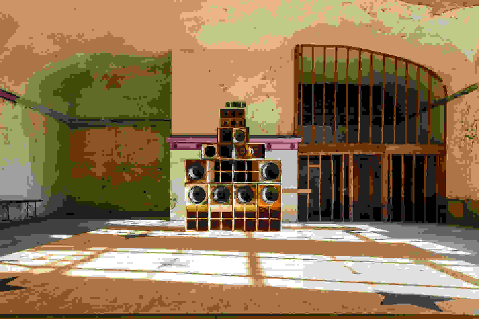 <p "="">A stack of speakers made with salvaged materials stands in an empty warehouse on a plywood platform painted with large black stars.