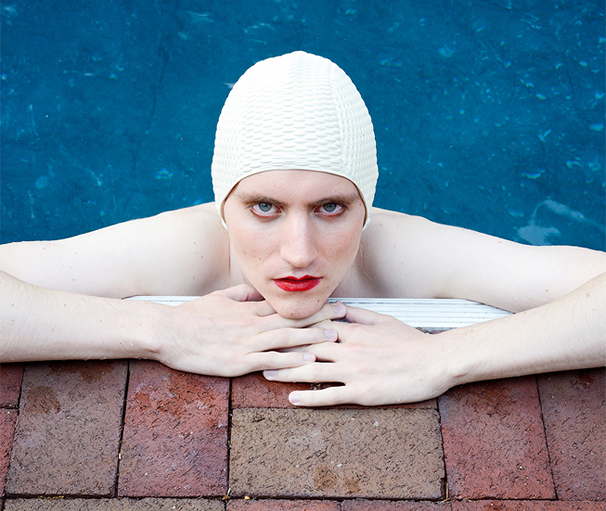 <p "="">A photograph of a person in a swimming cap, resting at the edge of a pool.