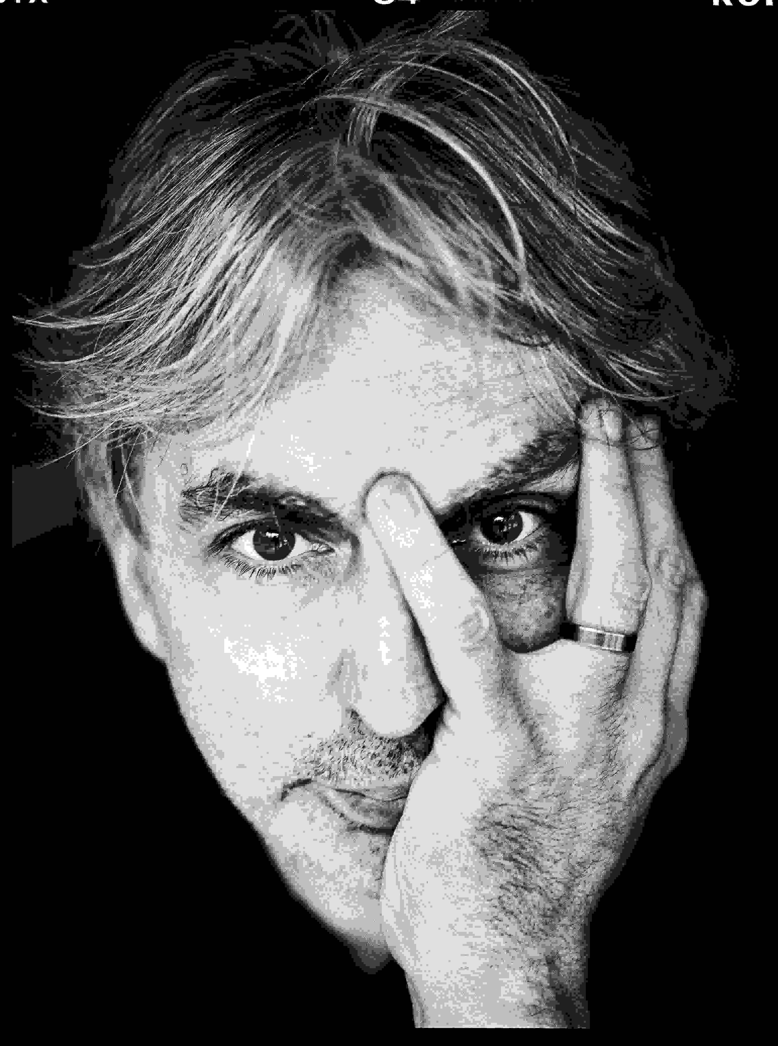 A black-and-white photograph of a man holding his head in his left hand and staring at the camera.