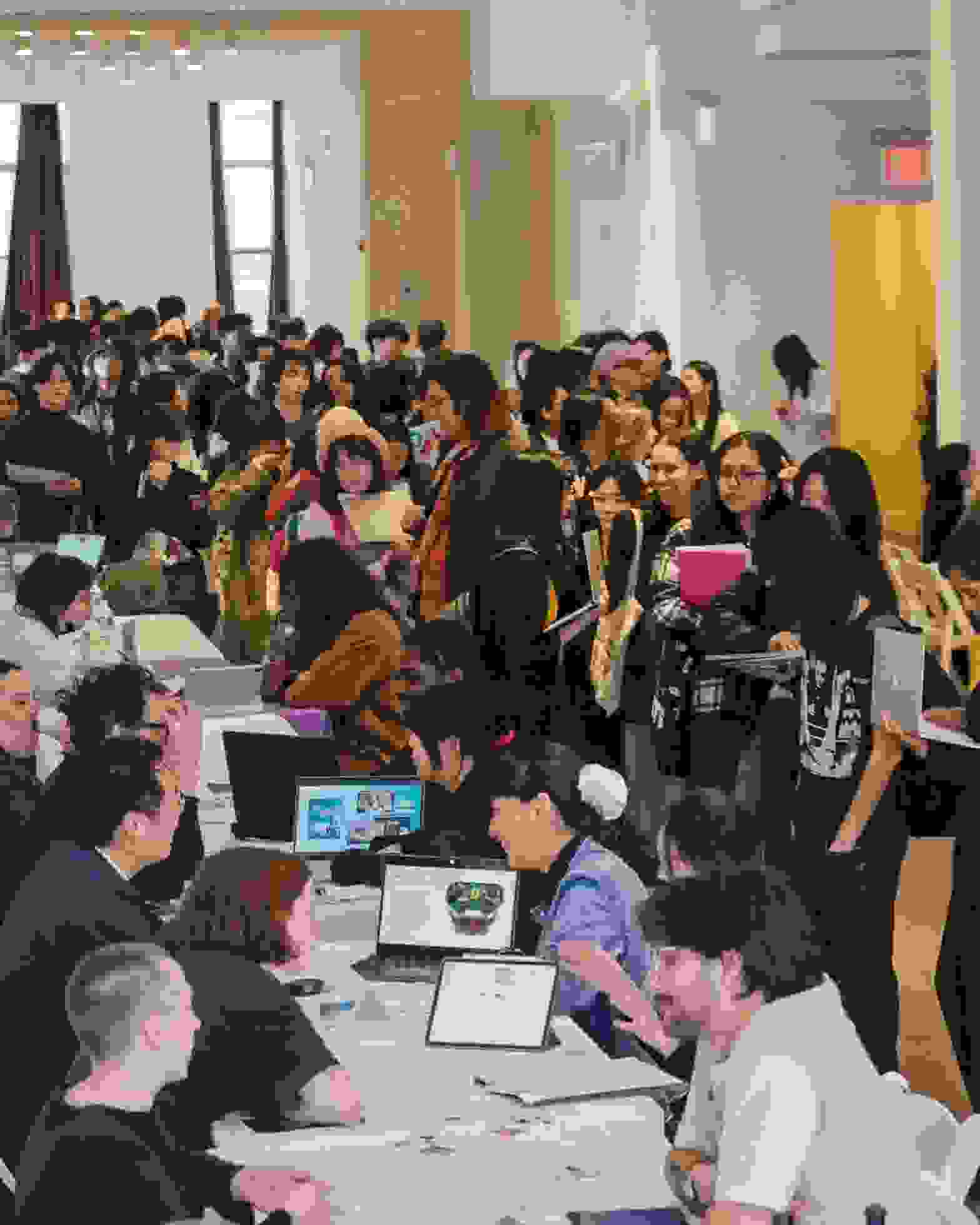 A highly attended career fair event in a large room wherein students mill about from table to table talking to prospective employers