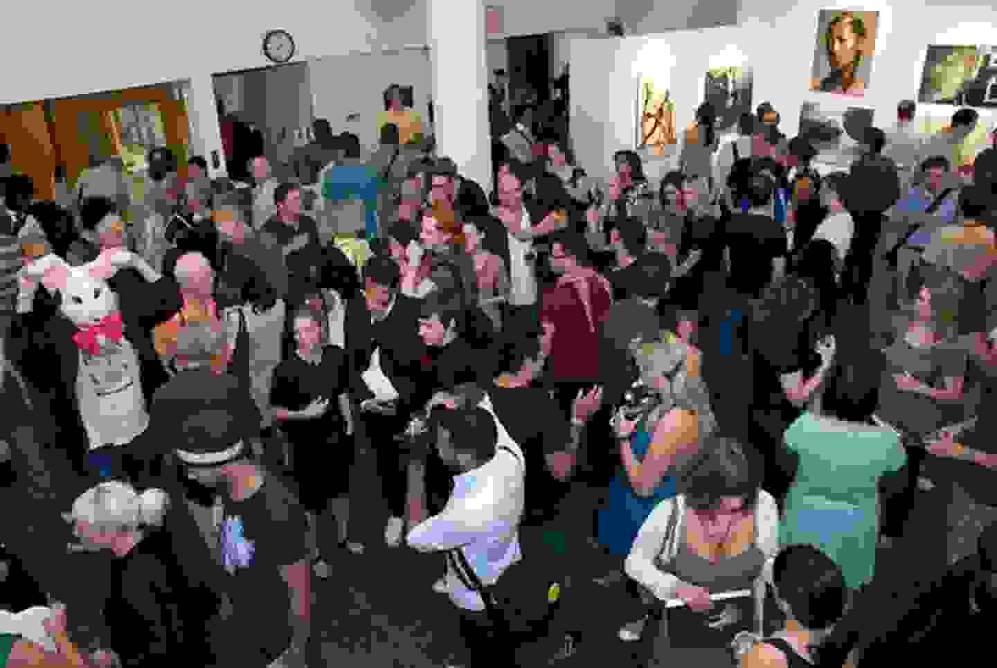 Bird’s eye view of a exhibition opening reception; many people filtering through the gallery space at 209 e 23rd