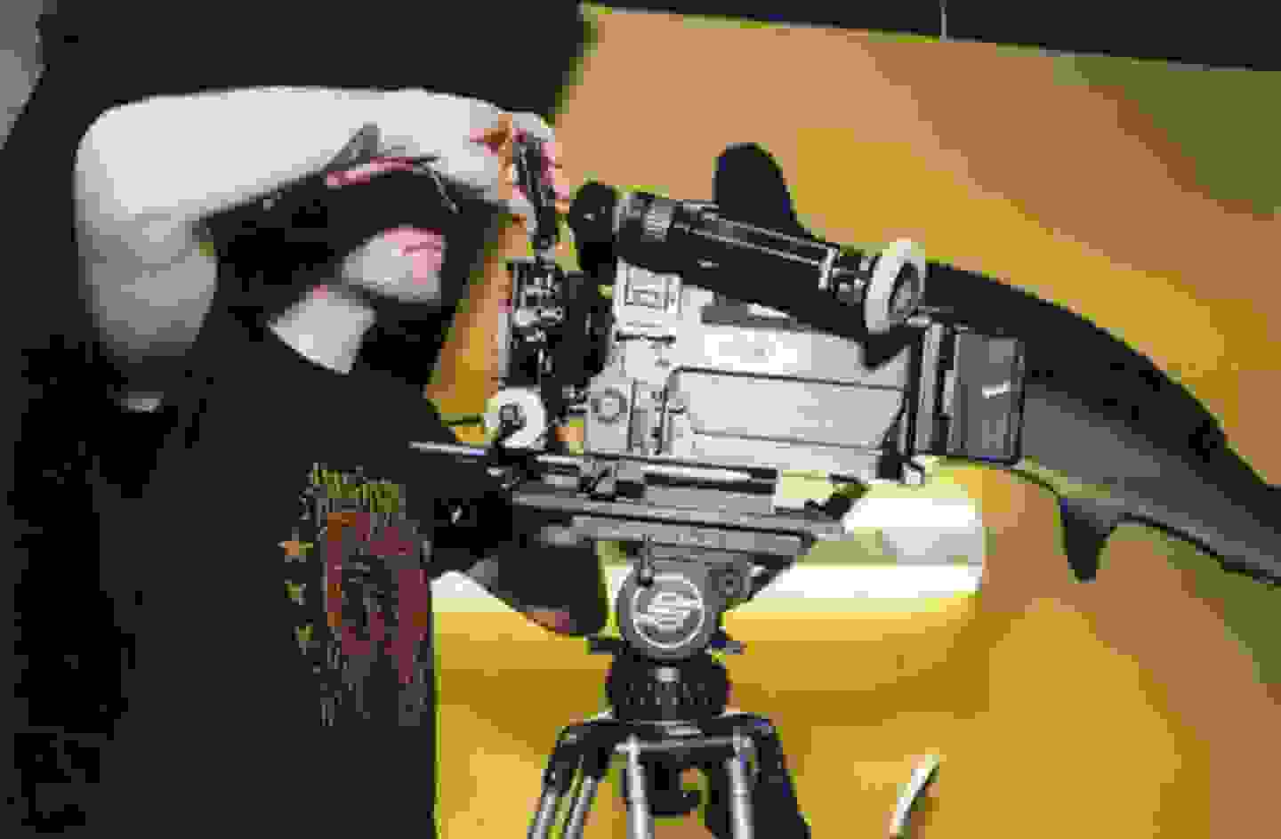 Person in a graphic t-shirt operating a video camera on a tripod
