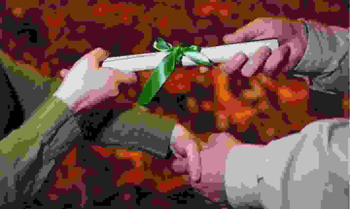 A close up of an administrator handing a diploma to someone; a white scroll fastened with a green ribbon