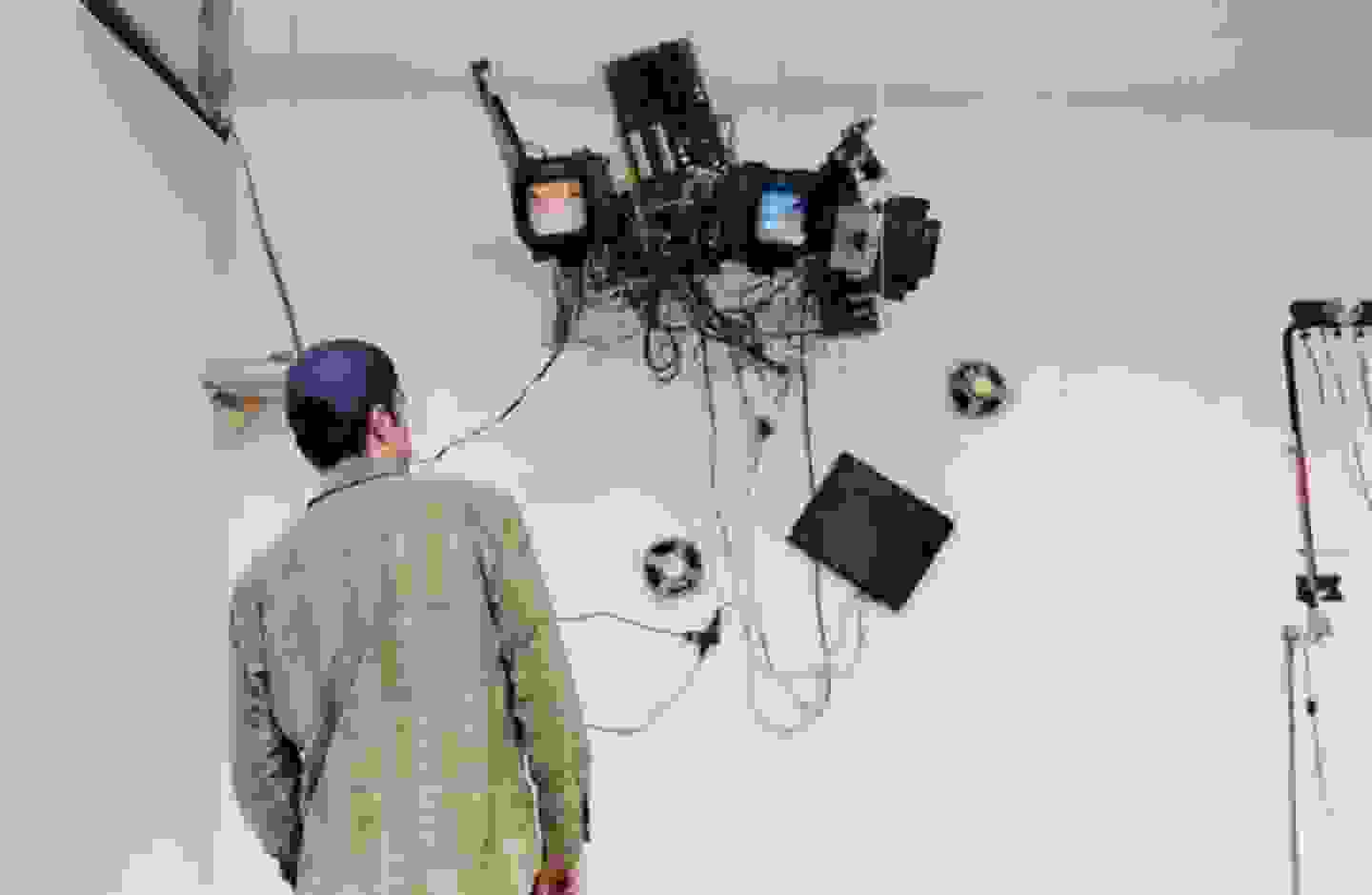 Person with back to the camera in the foreground; behind them, a mixed media assemblage suspended from the ceiling