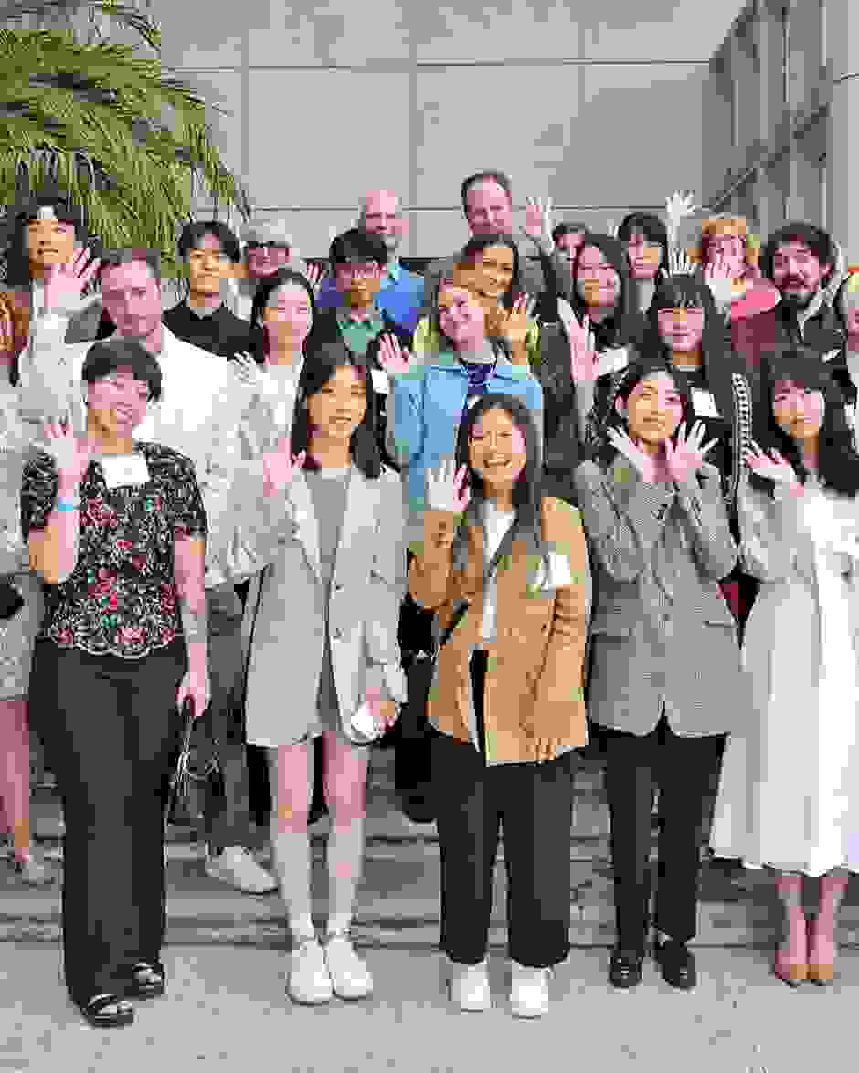 A group of graduates from SVA's class of 2022 and SVA staff members pose in on a set of stairs, smiling and waving at the camera.
